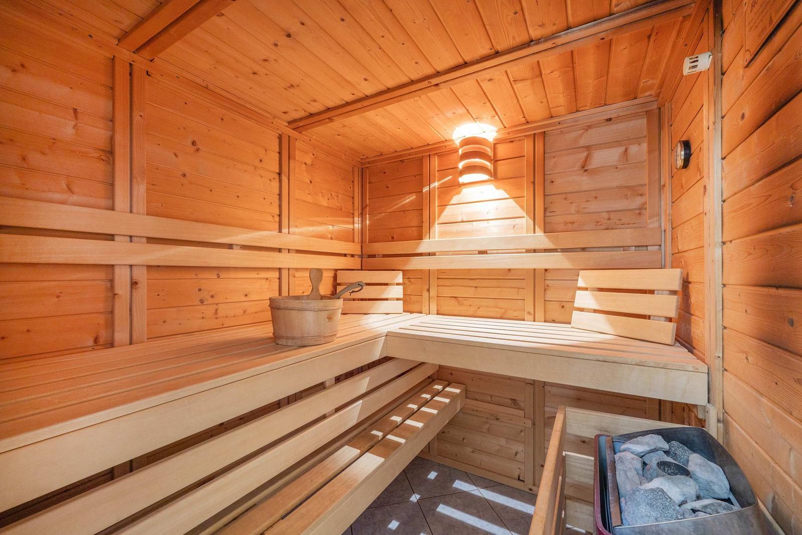 Holzsauna mit Sitzbänken, Eimer und Steinen.