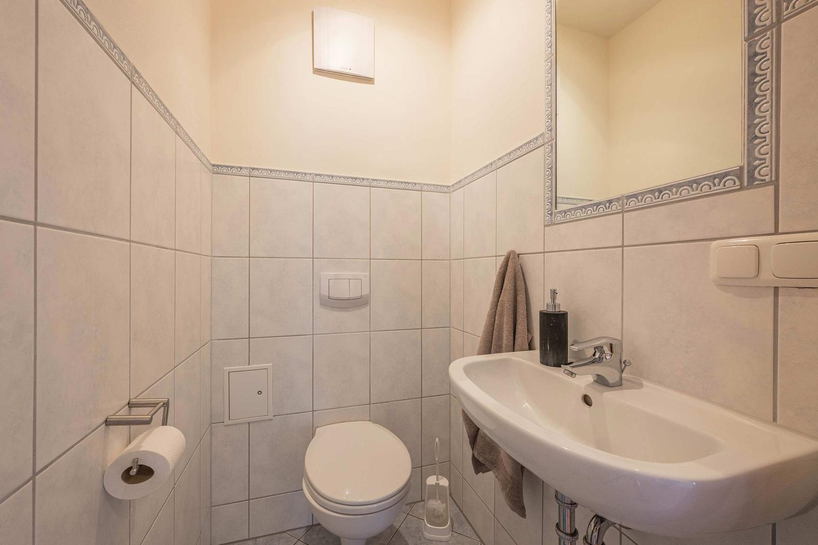 Badezimmer mit Toilette, Waschbecken und Spiegel. Wandfliesen mit Verzierung.