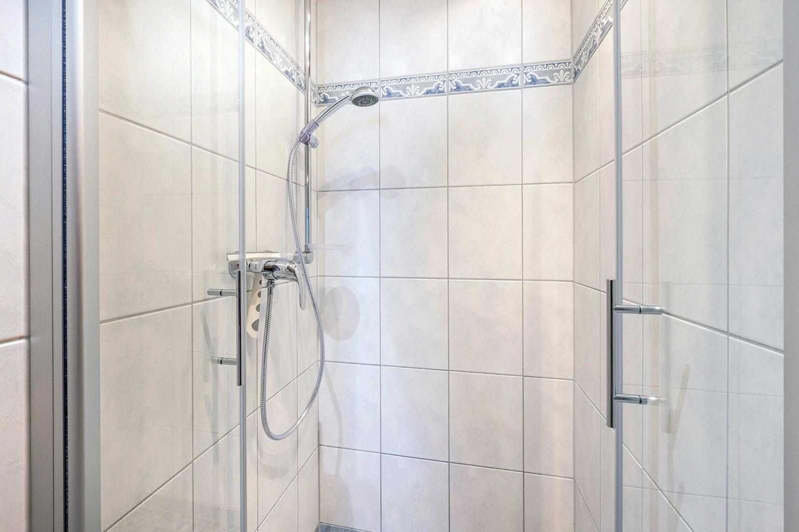 Dusche mit Glaswand, weißen Fliesen und blau-weißem Zierband.