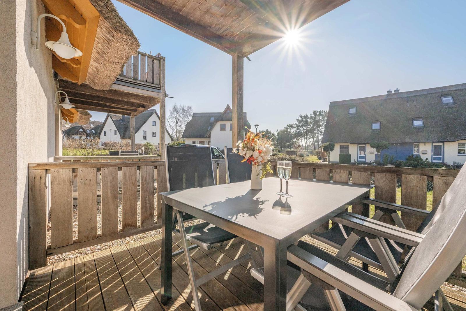 Terrasse mit Tisch, Stühlen und Blumenvase unter Sonne.