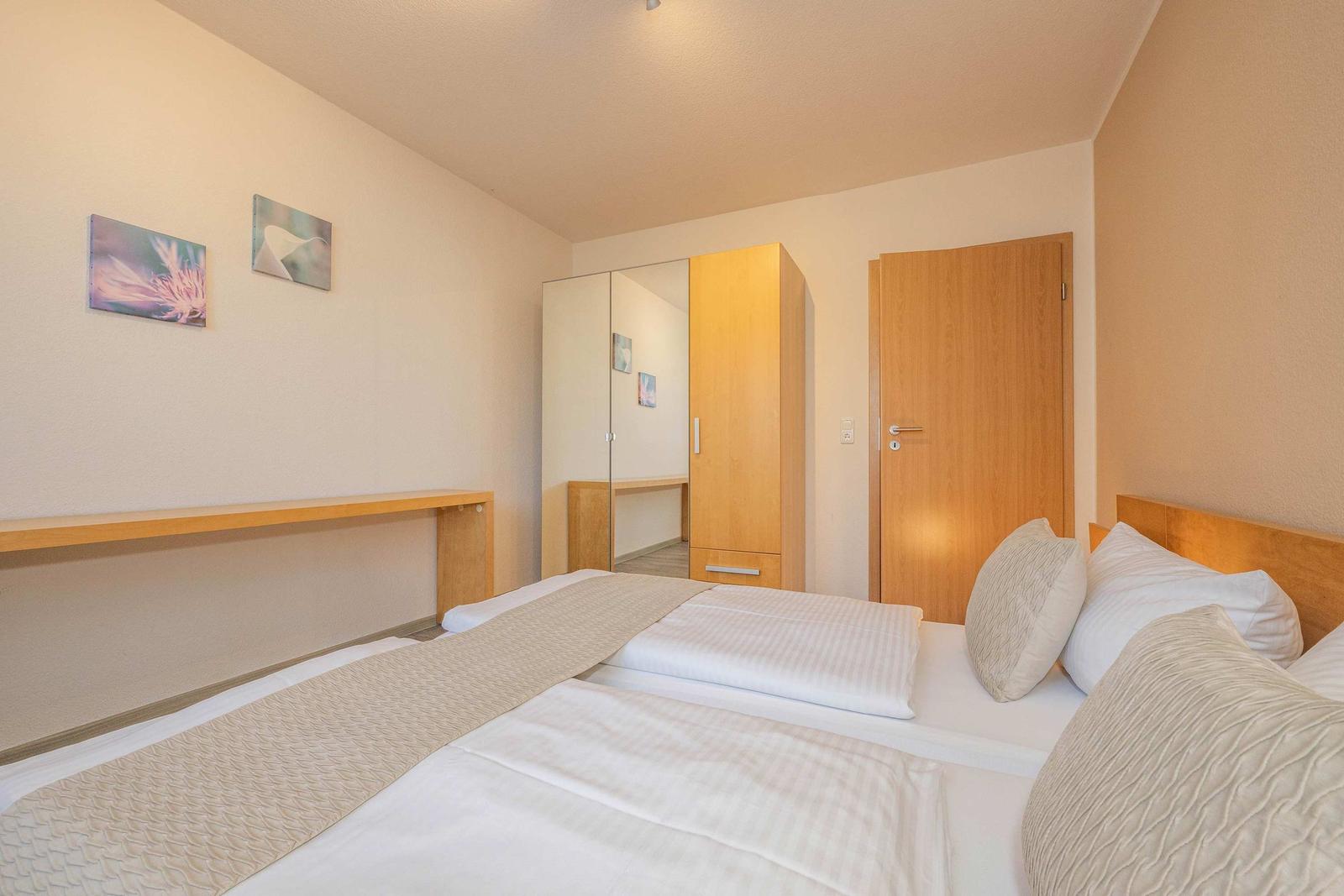 Schlafzimmer mit Bett, Kleiderschrank und Wandbildern.