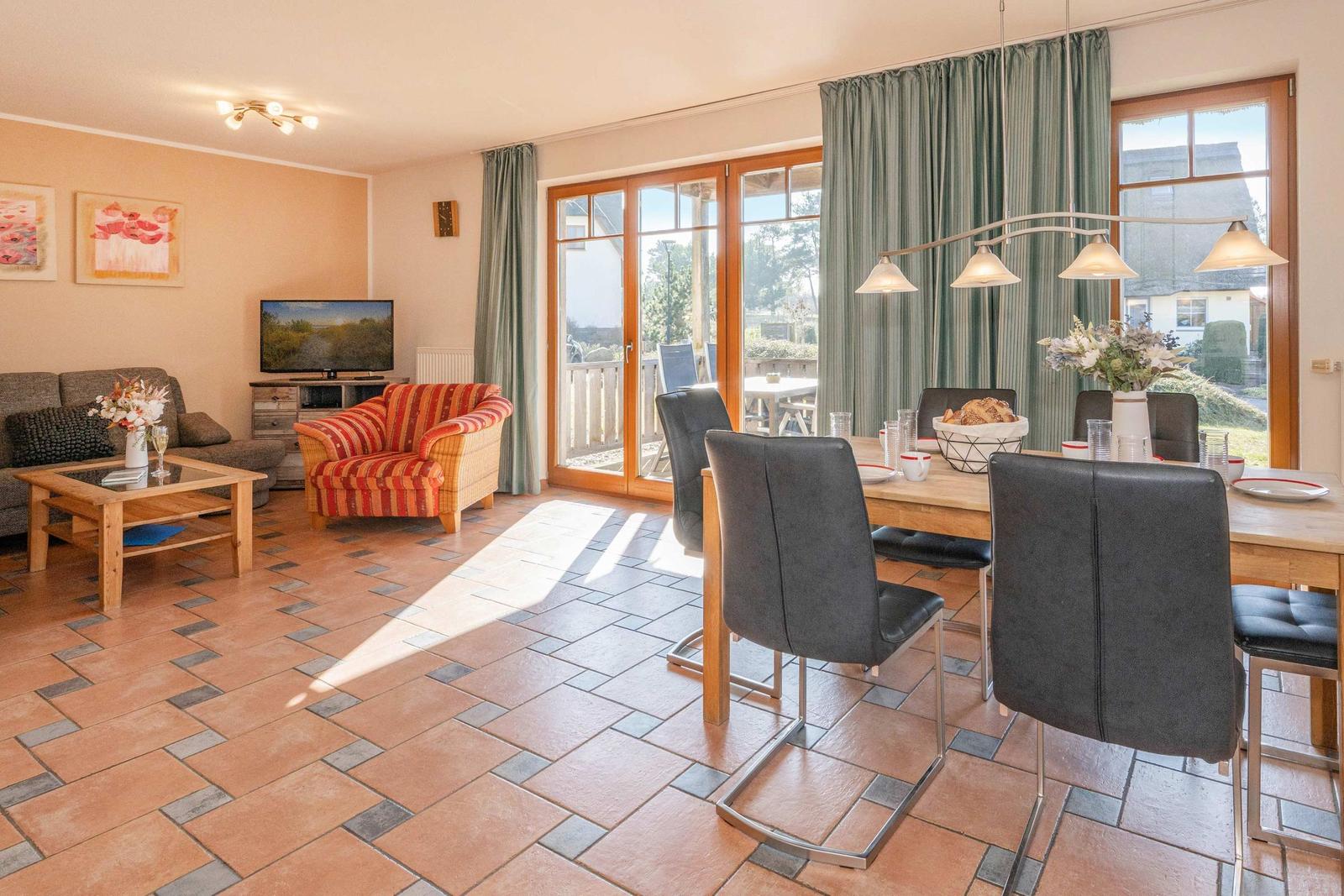 Wohn- und Essbereich mit Terrasse, Esstisch, Sofa und Stühlen. Terrassenzugang durch Glastüren.