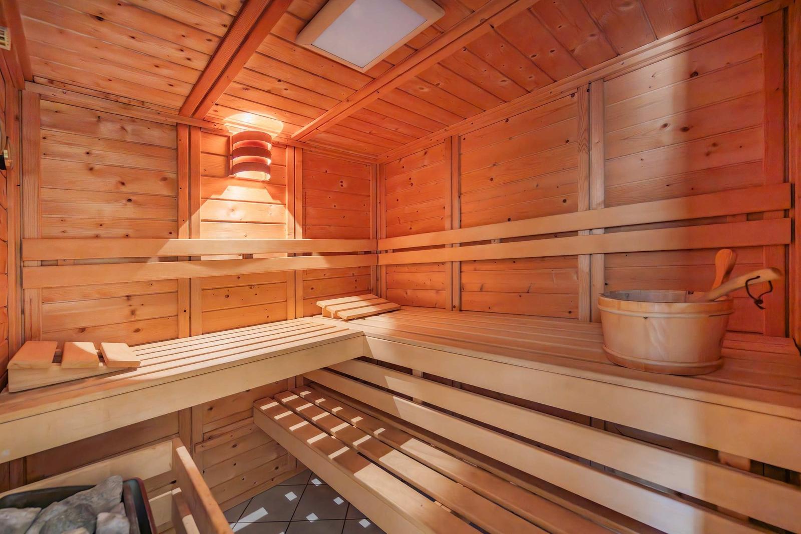 Holzsauna mit mehreren Sitzbänken und einem Eimer mit Löffel.