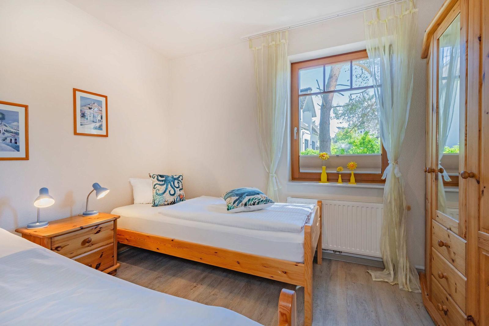 Ein Schlafzimmer mit zwei Betten, Holzmöbeln und einem Fenster mit Blick auf Bäume.