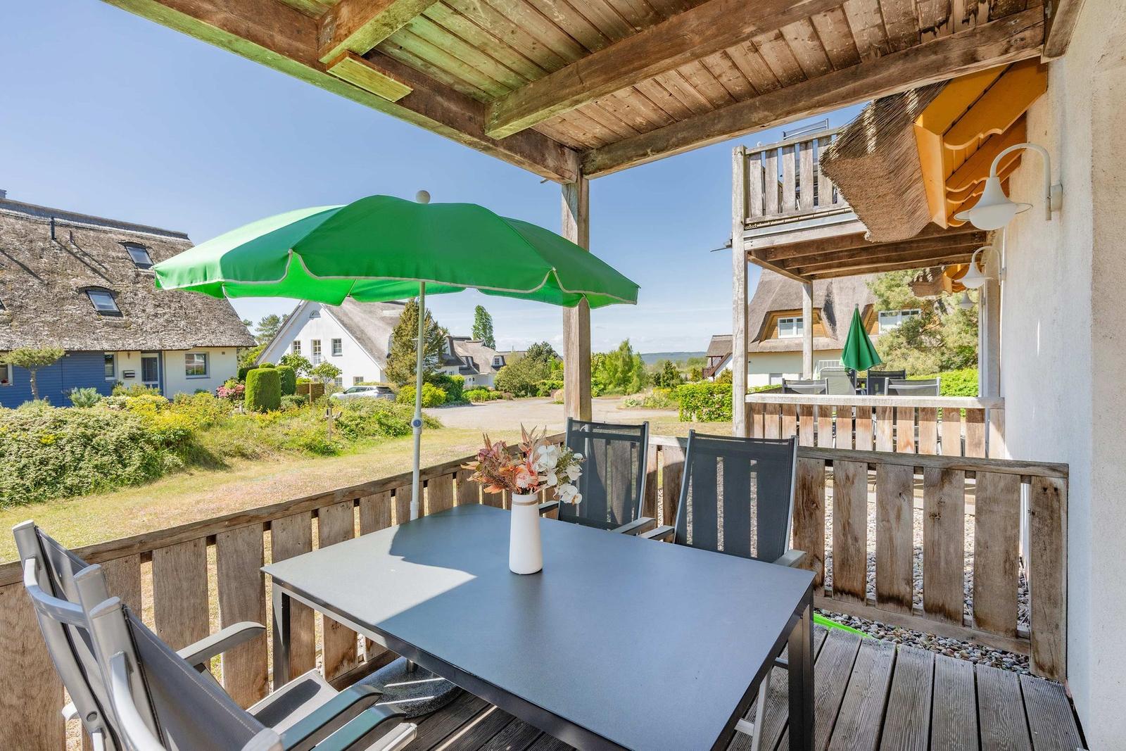 Terrasse mit Tisch, Stühlen und grünem Sonnenschirm. Blick auf Dächer und Grünflächen.
