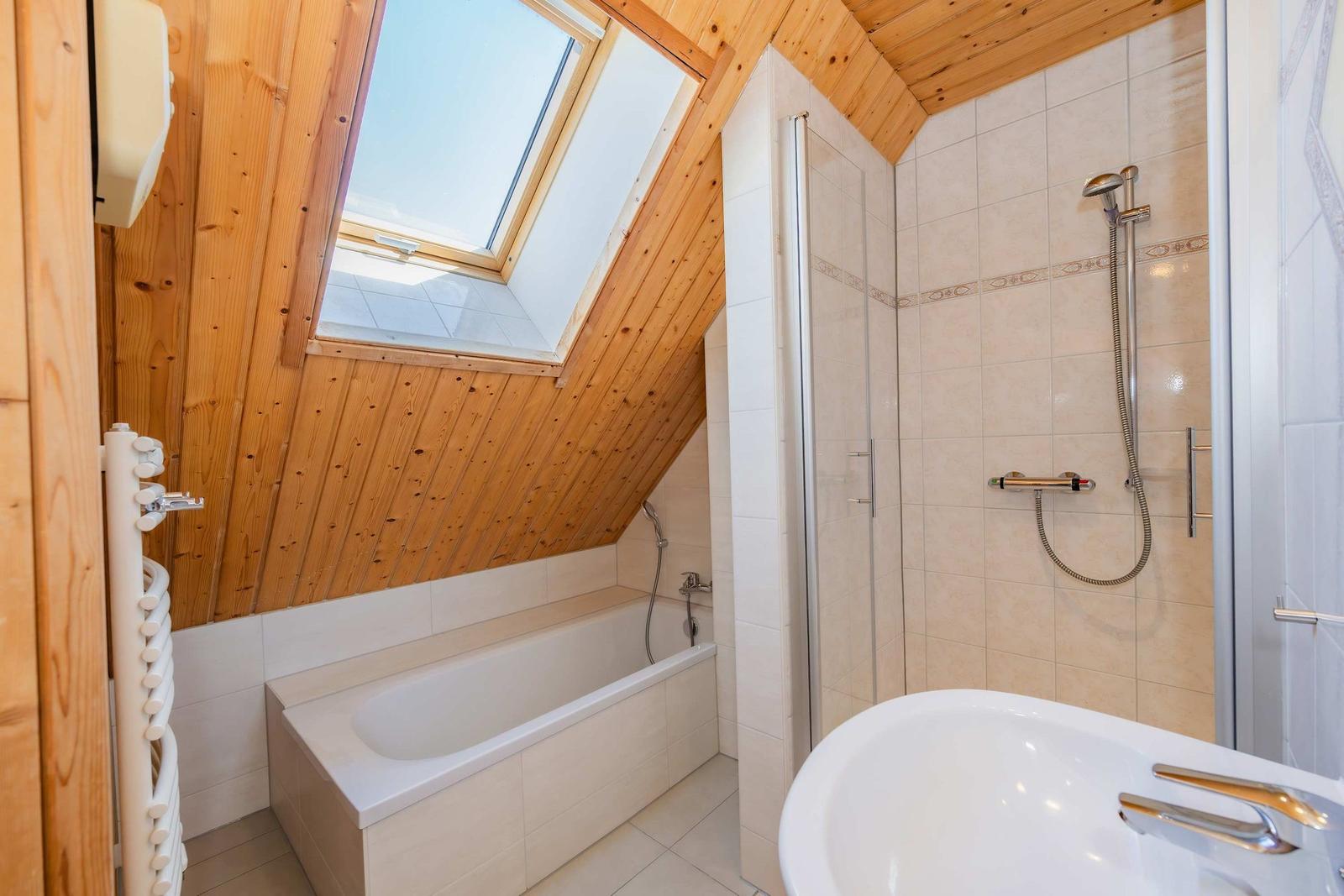 Badezimmer mit Dusche, Badewanne und Dachfenster. Holzdecke und Fliesenwand.