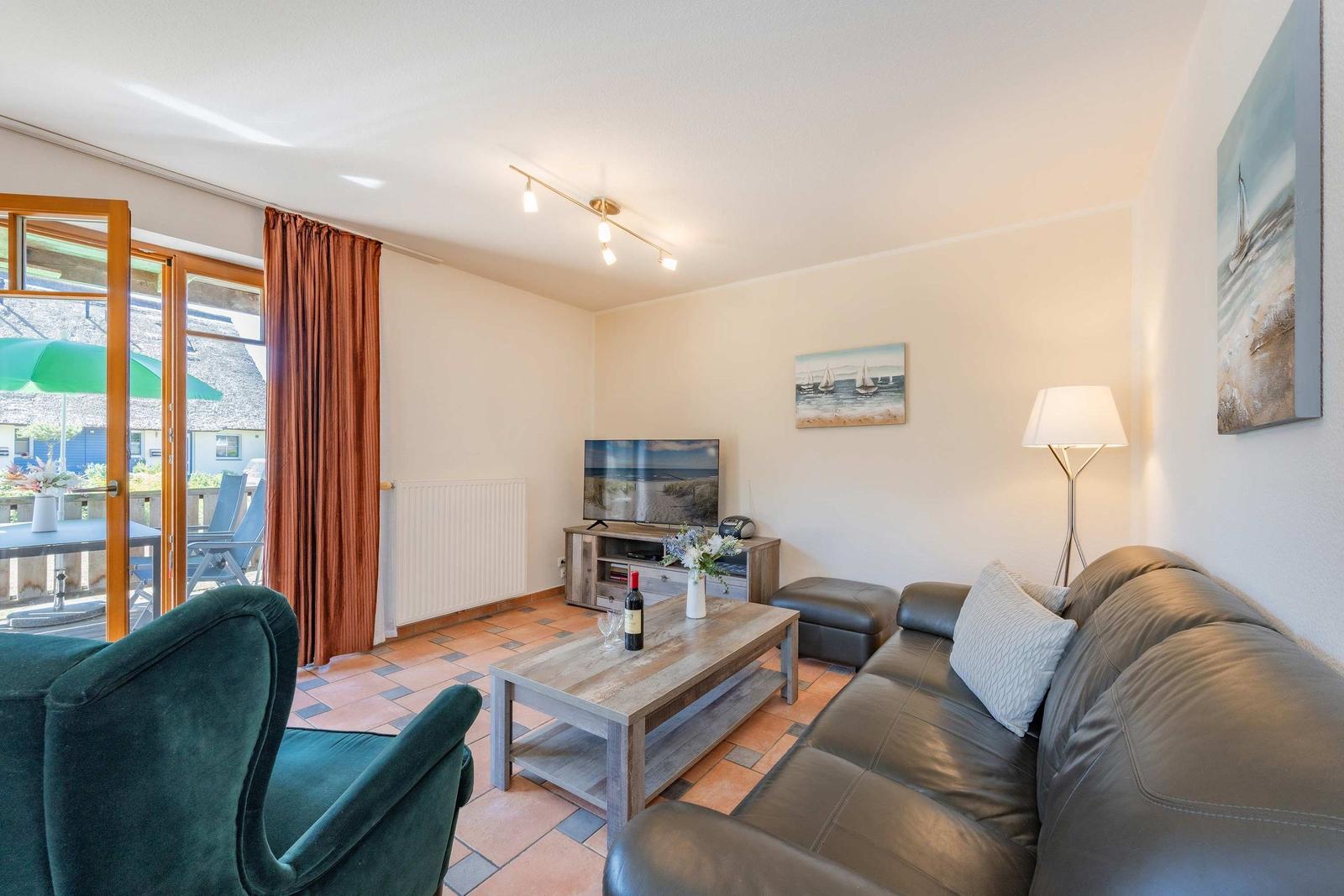 Wohnzimmer mit Sofa, Couchtisch und Fernseher. Terrasse mit Blick auf Strand.