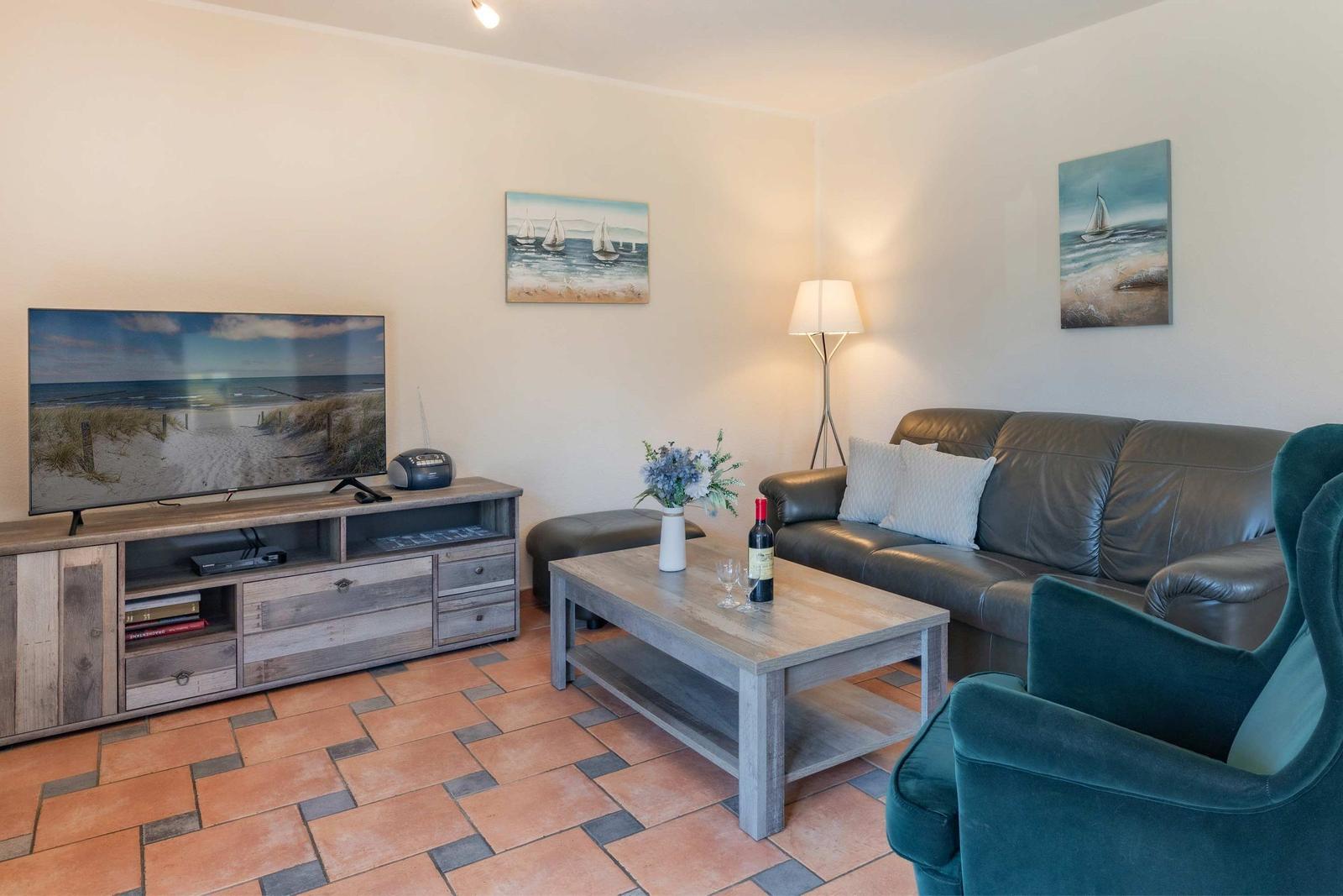 Wohnzimmer mit Sofa, Fernseher und Holztisch. Wandbilder zeigen Segelboote.