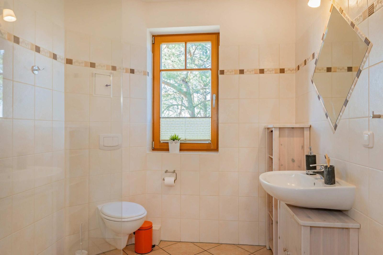 Badezimmer mit Toilette, Waschbecken und Dusche. Fenster mit Blick auf Bäume.
