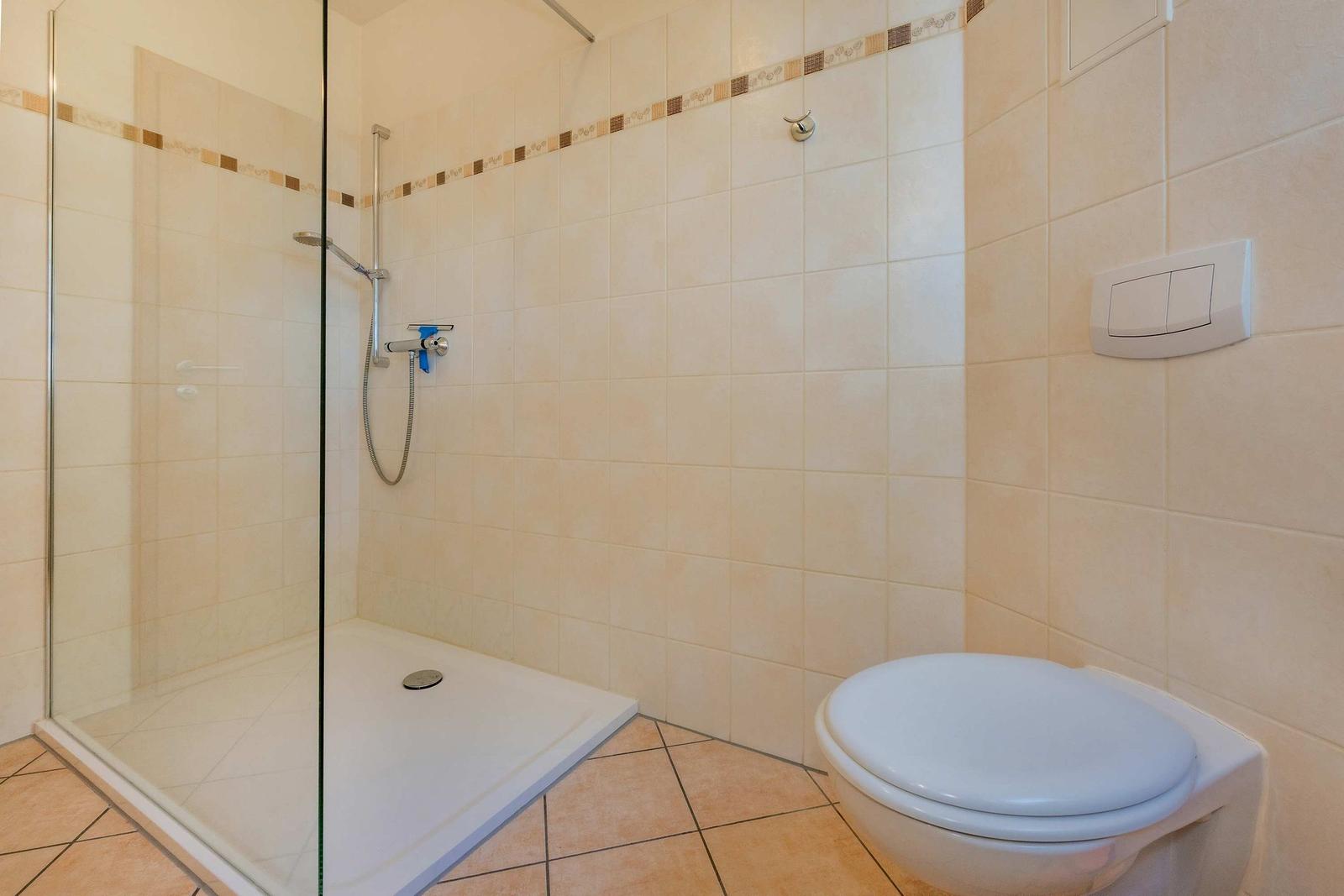 Dusche mit Glaswand, Toilette und Fliesenwand im Badezimmer.