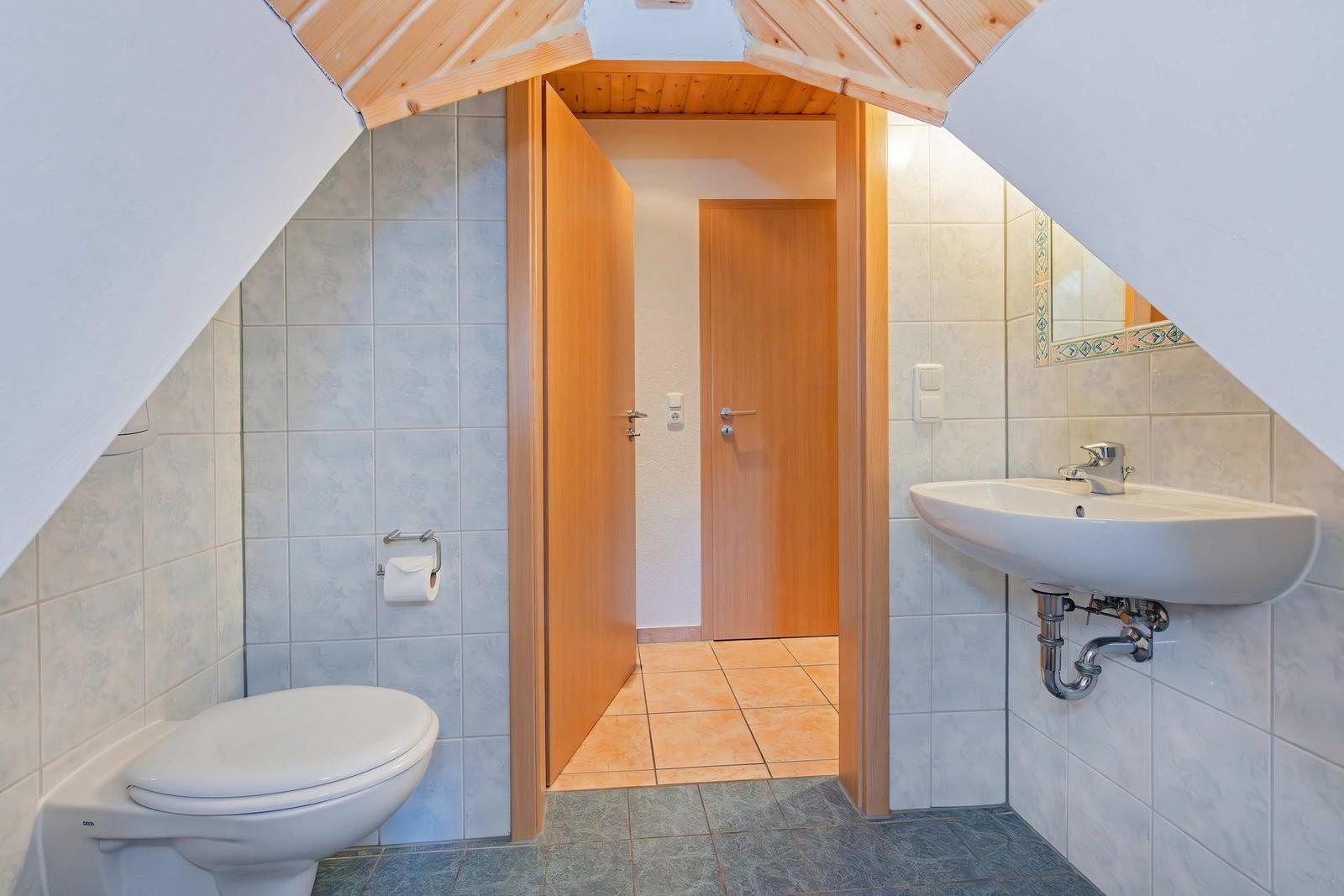 Badezimmer mit Toilette, Waschbecken und Dusche unter Dachschrägen.