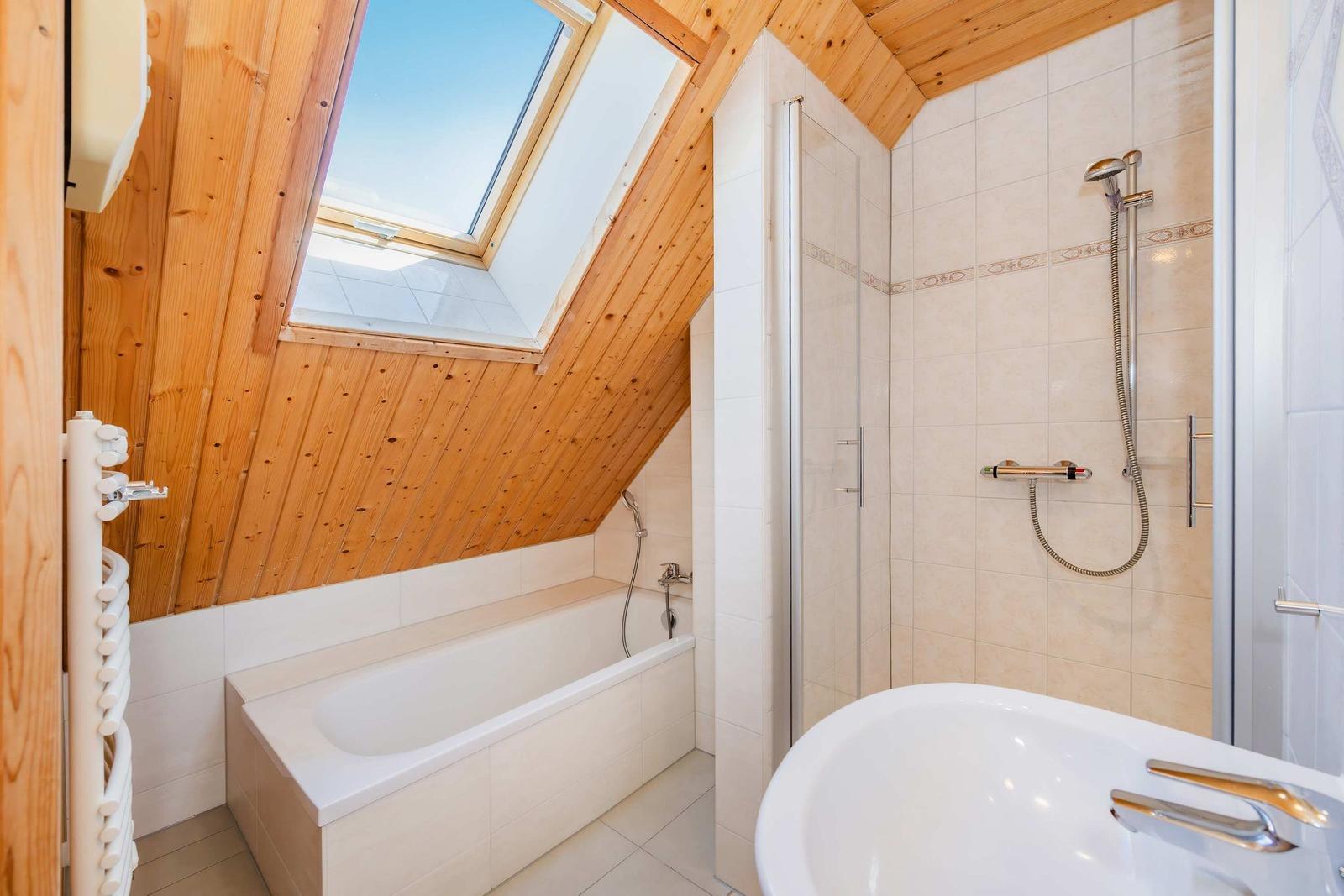 Badezimmer mit Dusche, Badewanne und Dachfenster. Holzdecke und Fliesenwand.