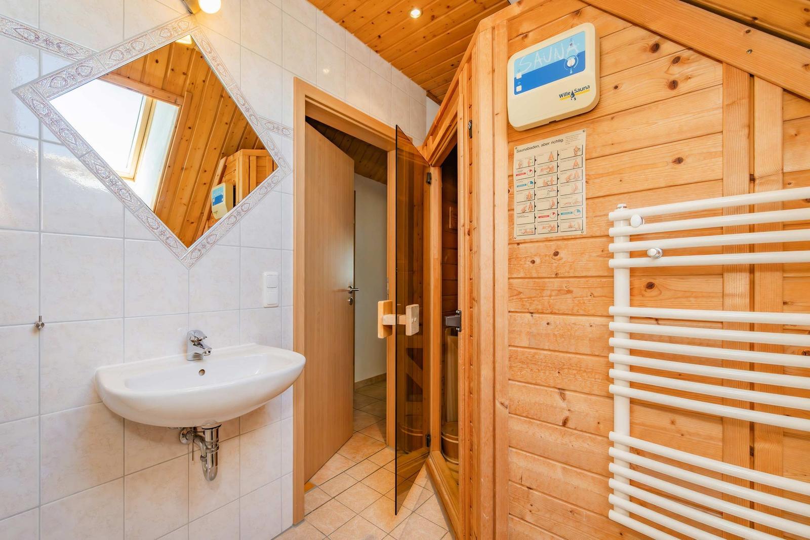 Bad mit Waschbecken, Spiegel und Sauna mit Heizung und Handtuchhalter.