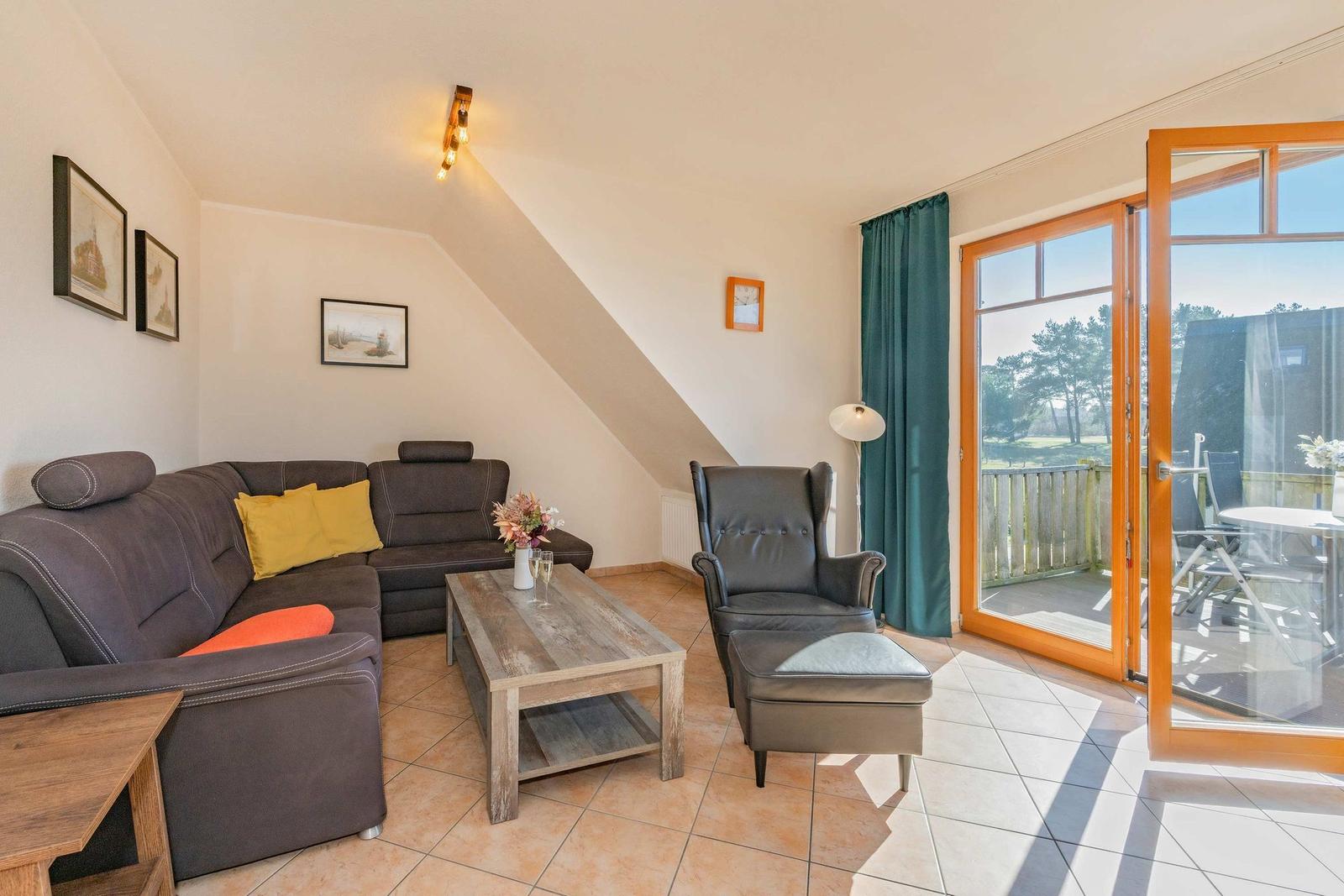 Wohnzimmer mit Sofa, Sessel und Terrasse. Durchgang zur Terrasse mit Tisch und Stühlen.
