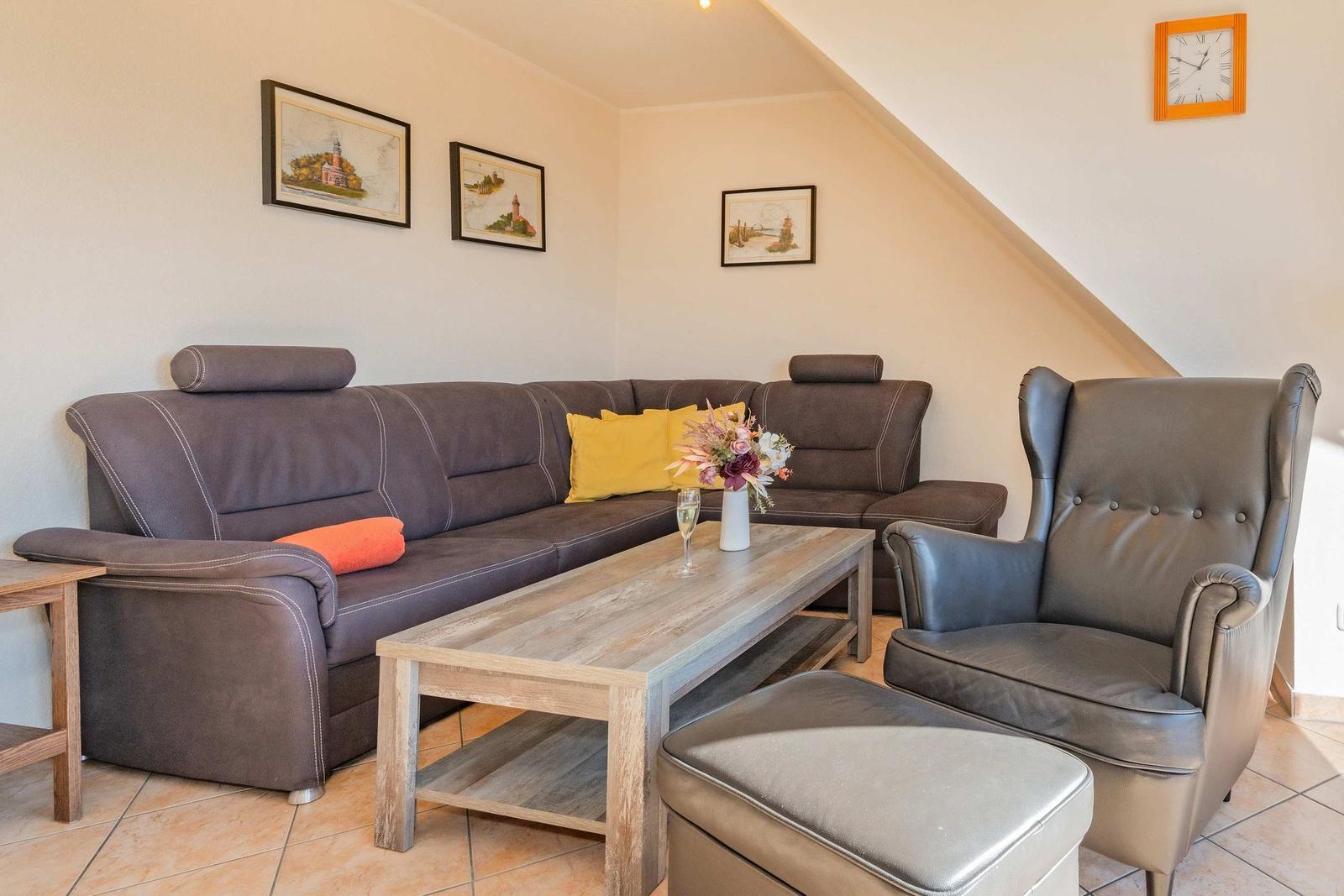 Wohnzimmer mit Sofa, Sessel und Couchtisch. Wandbilder und Uhr an der Wand.
