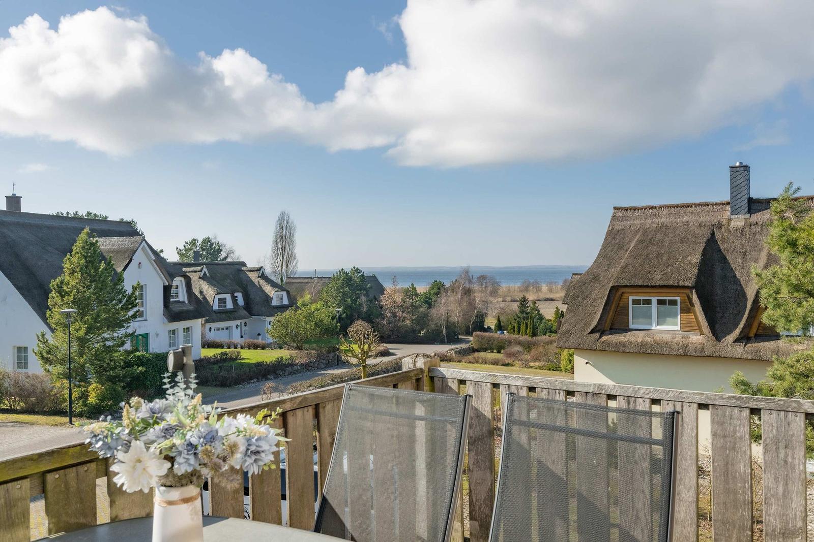 Terrasse mit Blick auf Dächer und Meer unter blauem Himmel mit weißen Wolken.
