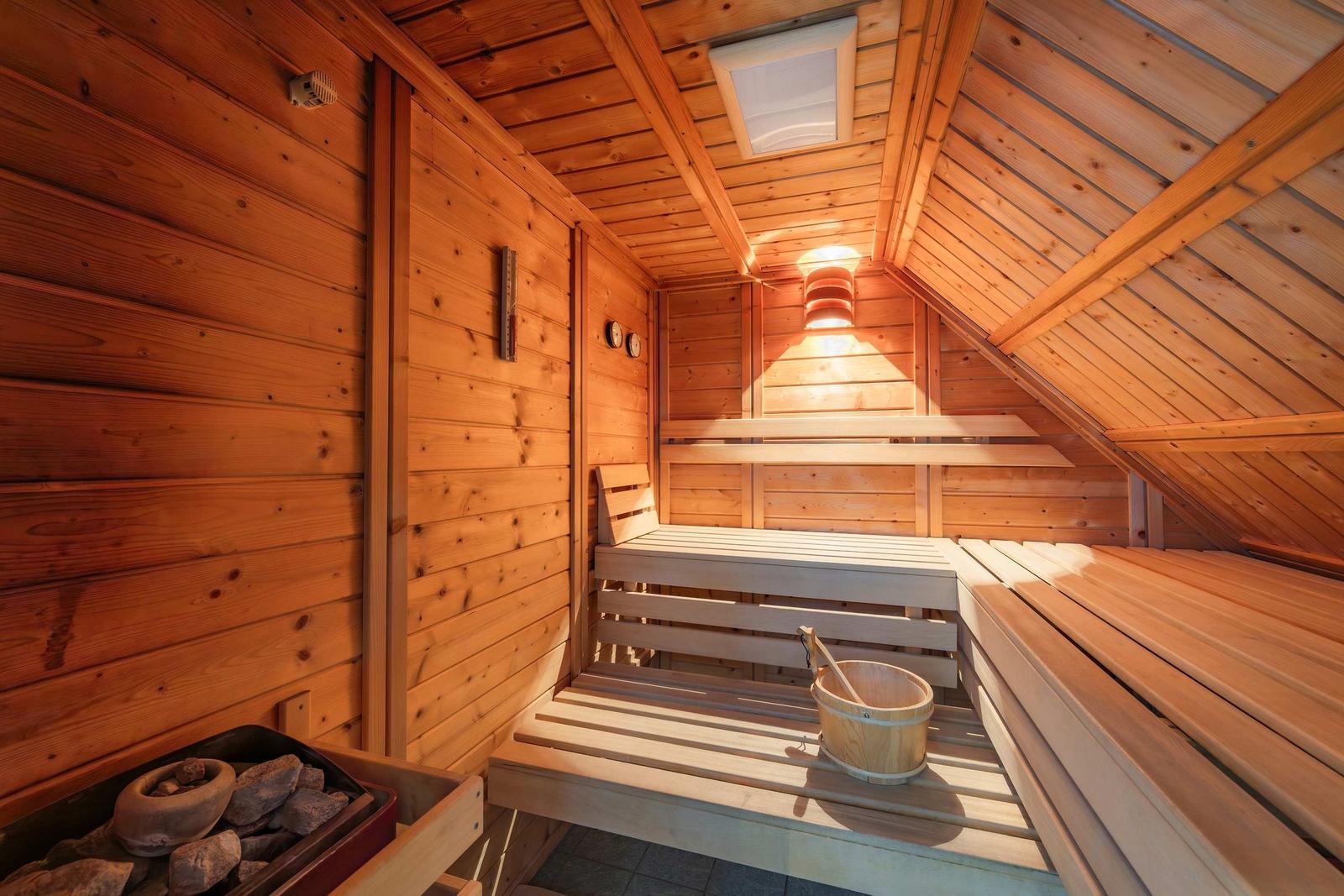 Sauna mit Holzbänken und Steinmulde. Decke mit Dachbodenstruktur.