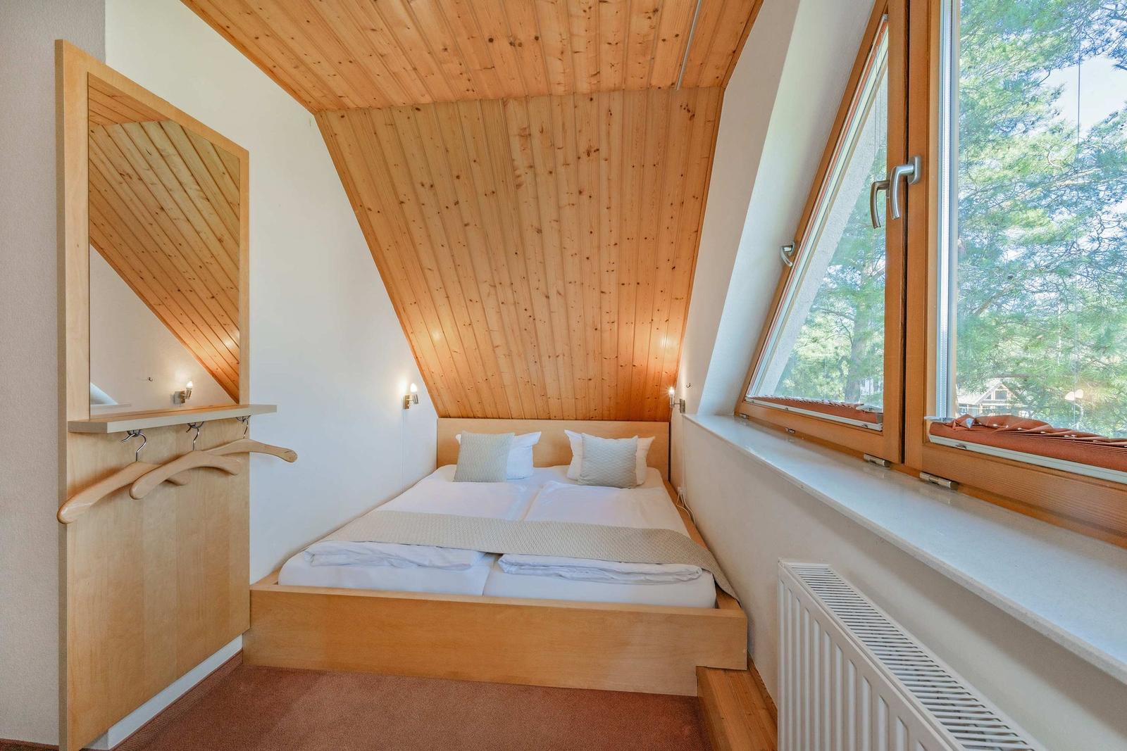 Schlafzimmer mit Holzdecke, Doppelbett und Fensterblick auf Bäume