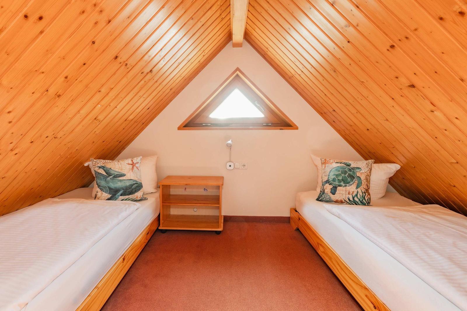 Zwei Betten unter Dachschräge mit Holzwand und Dreiecksfenster.