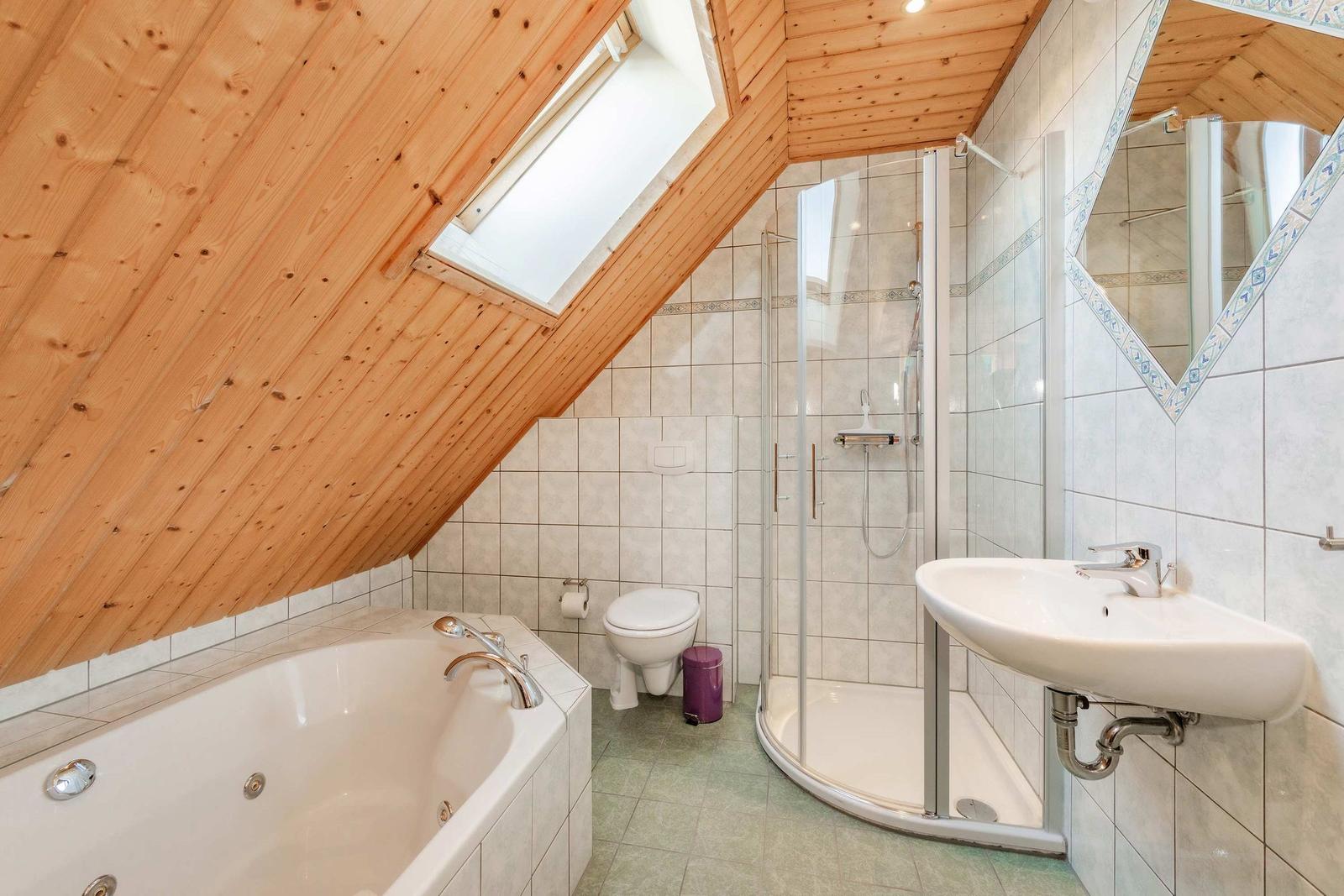 Badezimmer mit Dusche, Badewanne und Waschbecken unter Holzdecke.