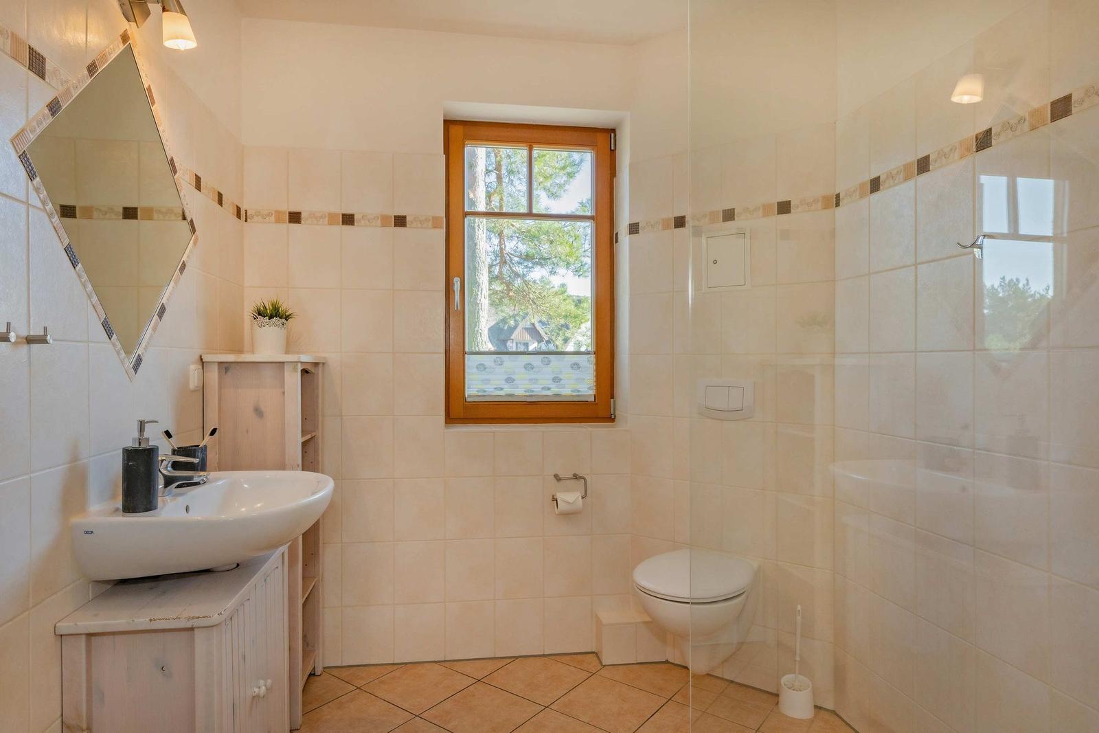 Badezimmer mit Waschbecken, Toilette und Dusche. Fenster mit Blick auf Bäume.
