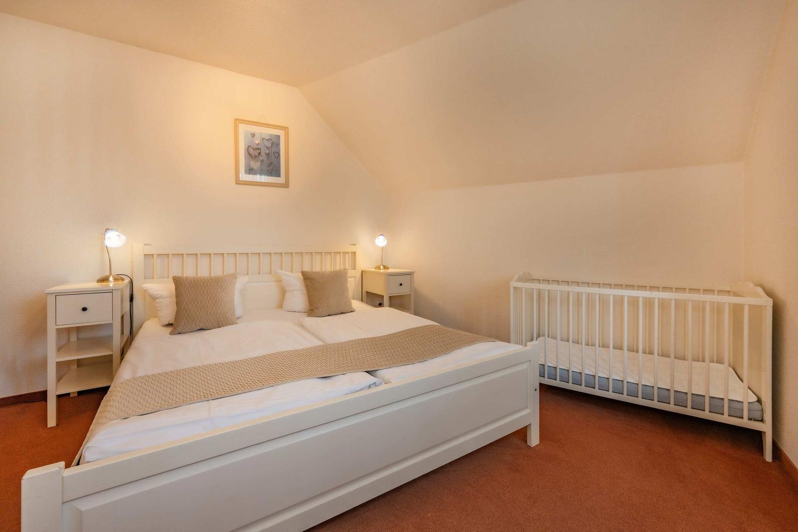 Schlafzimmer mit Doppelbett, Babybett und zwei Nachttischen mit Lampen.