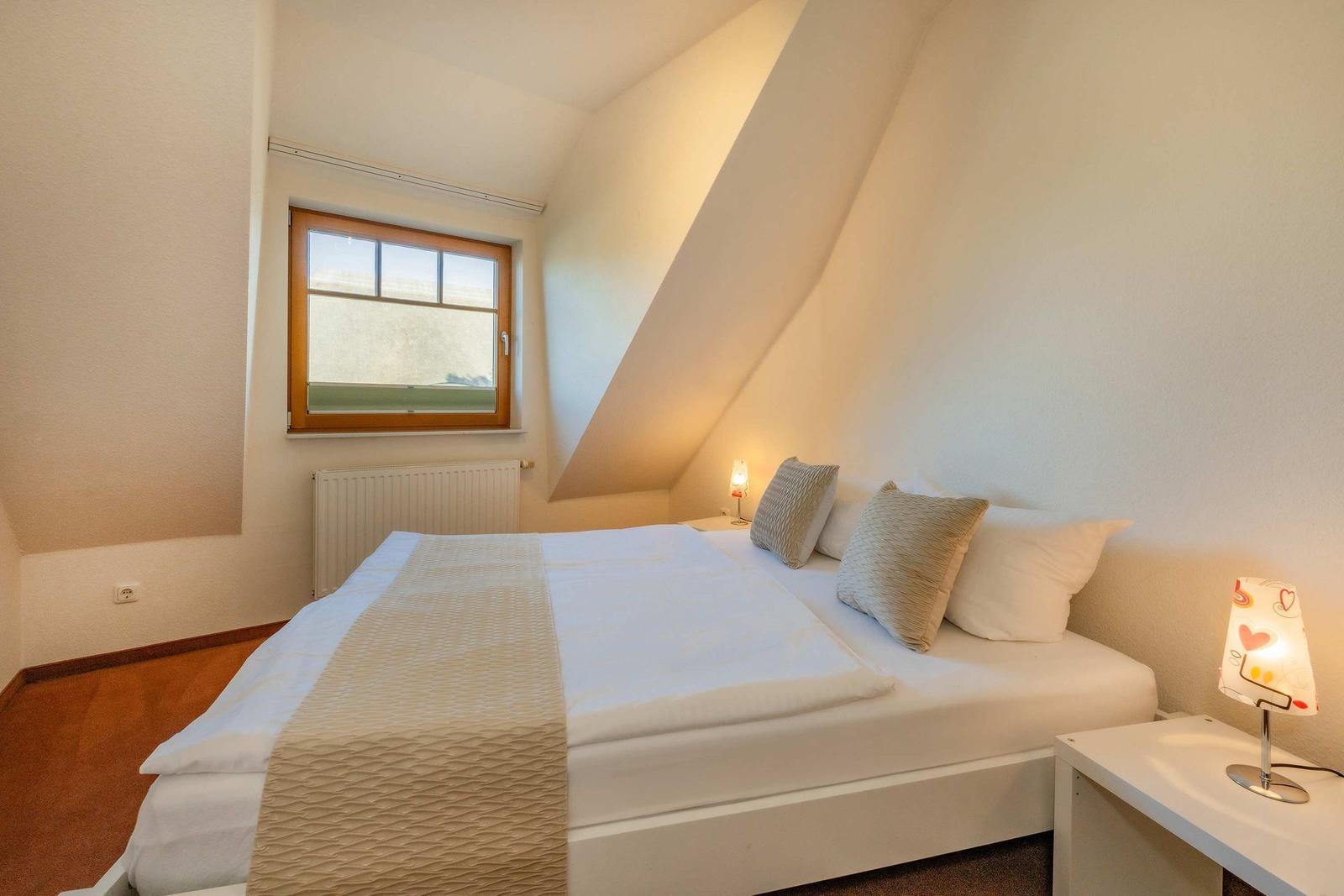 Schlafzimmer mit Dachschrägen, Bett, Nachttisch und Fenster.