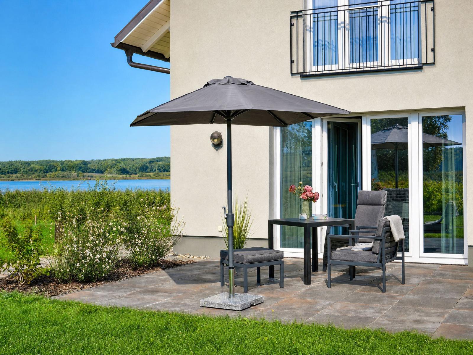 Terrasse mit Sonnenschirm, Tisch und Stühlen. Blick auf See und Wald.