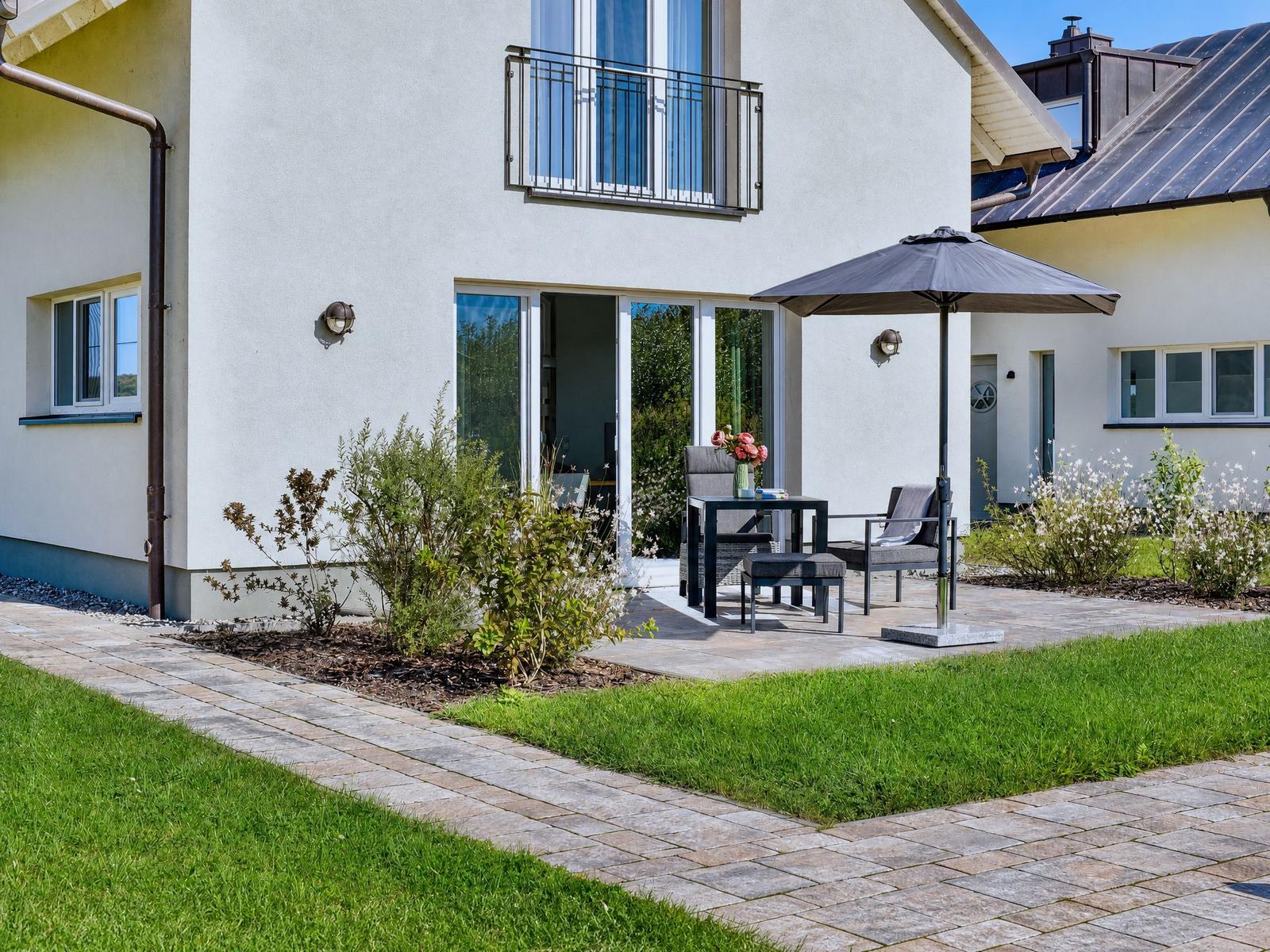 Haus mit Balkon, Terrasse und Sitzgelegenheit unter Sonnenschutz.