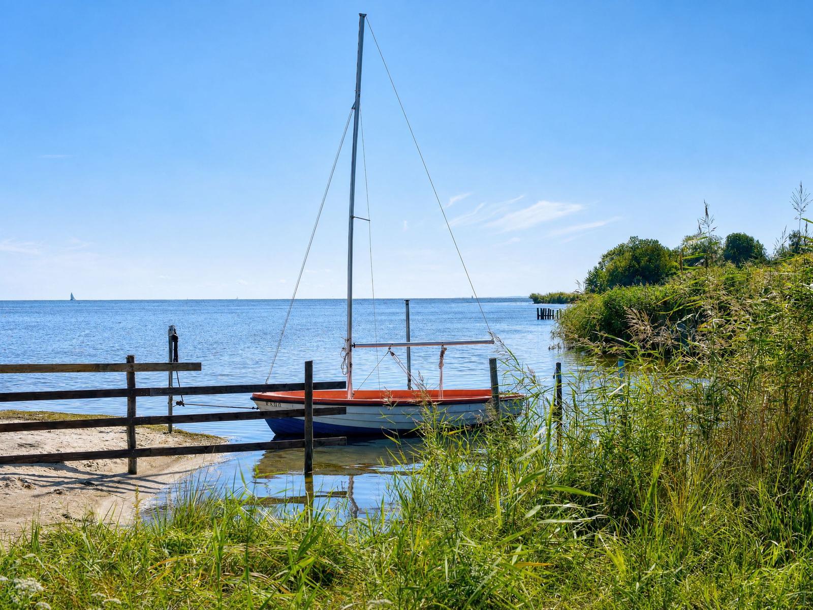Segelboot liegt am Ufer mit Gras und Holzgeländer.