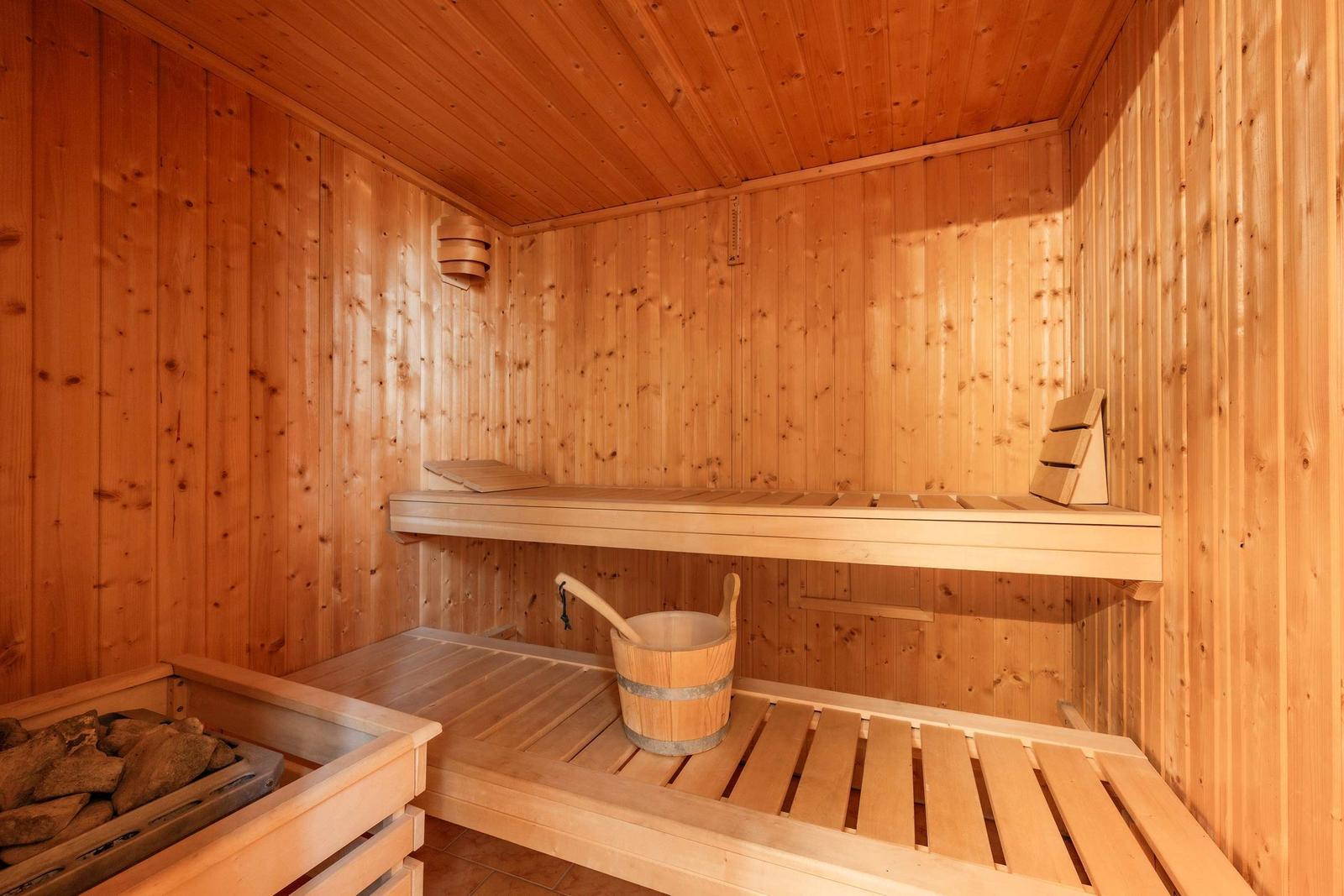 Holzsauna mit Bank, Eimer und Steinbecken.