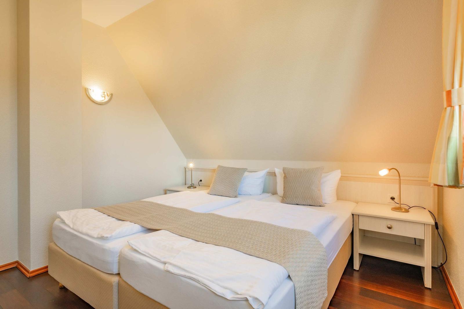 Schlafzimmer mit Doppelbett, Nachttisch und Wandlampe unter schräger Decke.