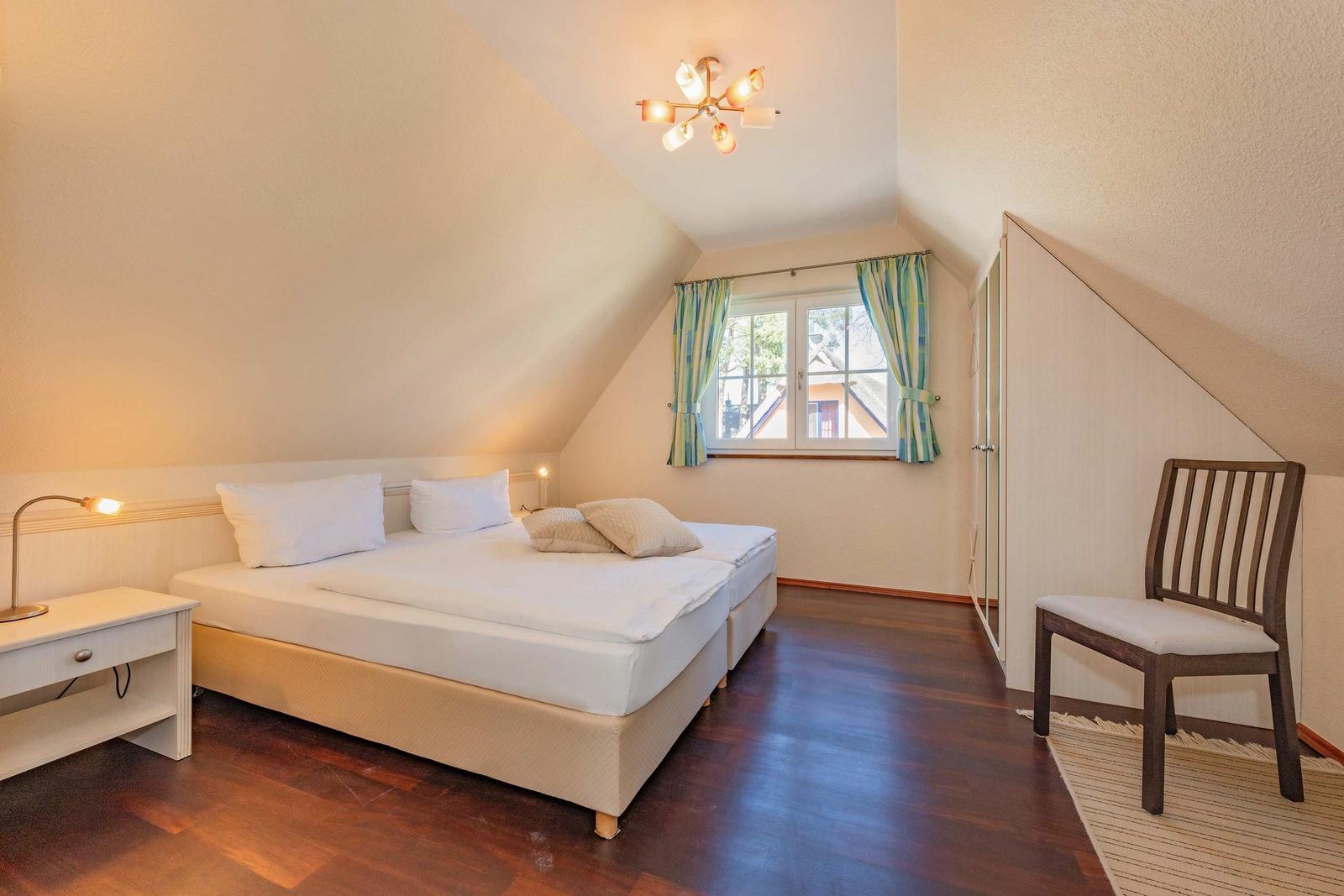 Schlafzimmer mit Doppelbett, Schreibtisch, Stuhl und Fenster mit Vorhängen.