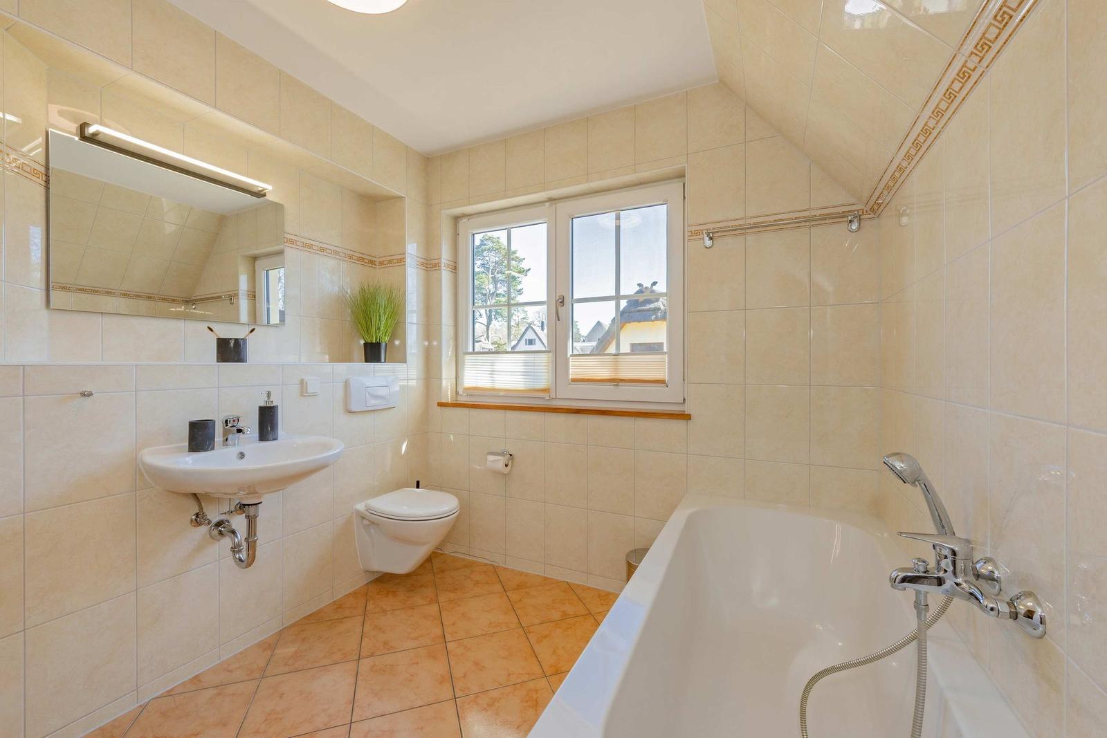 Badezimmer mit Badewanne, Waschbecken und Toilette. Fenster mit Blick nach draußen.