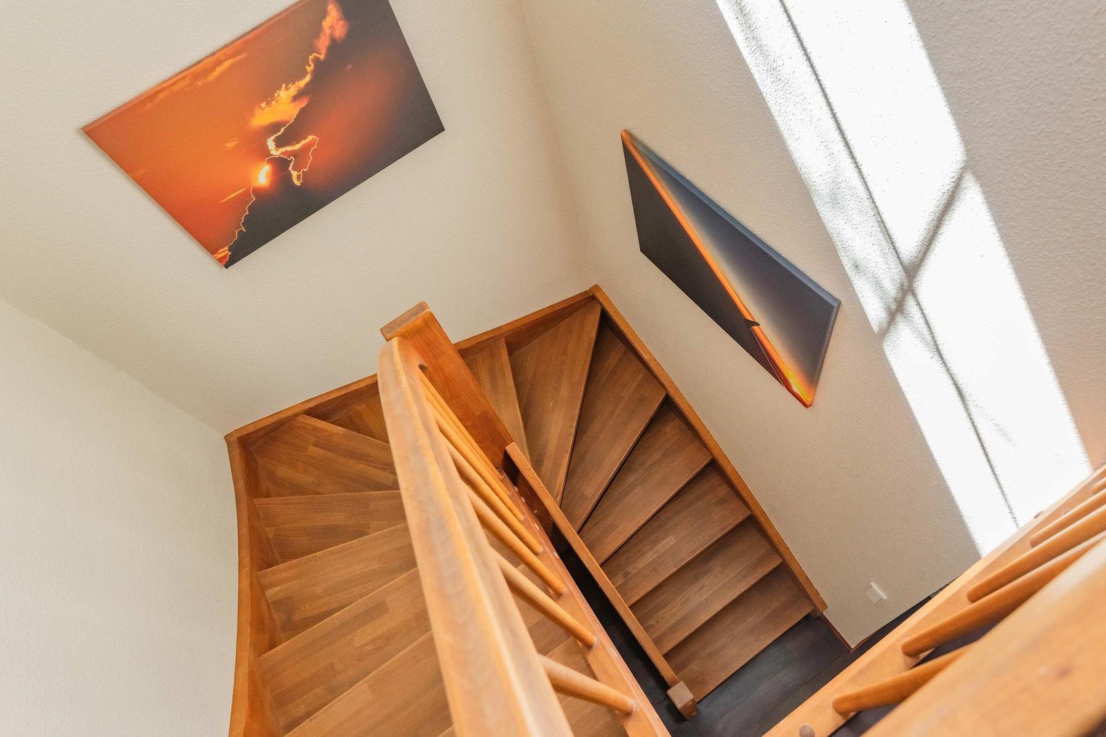 Holzgetreppe mit Geländer, Wandbilder und Fensterlicht.