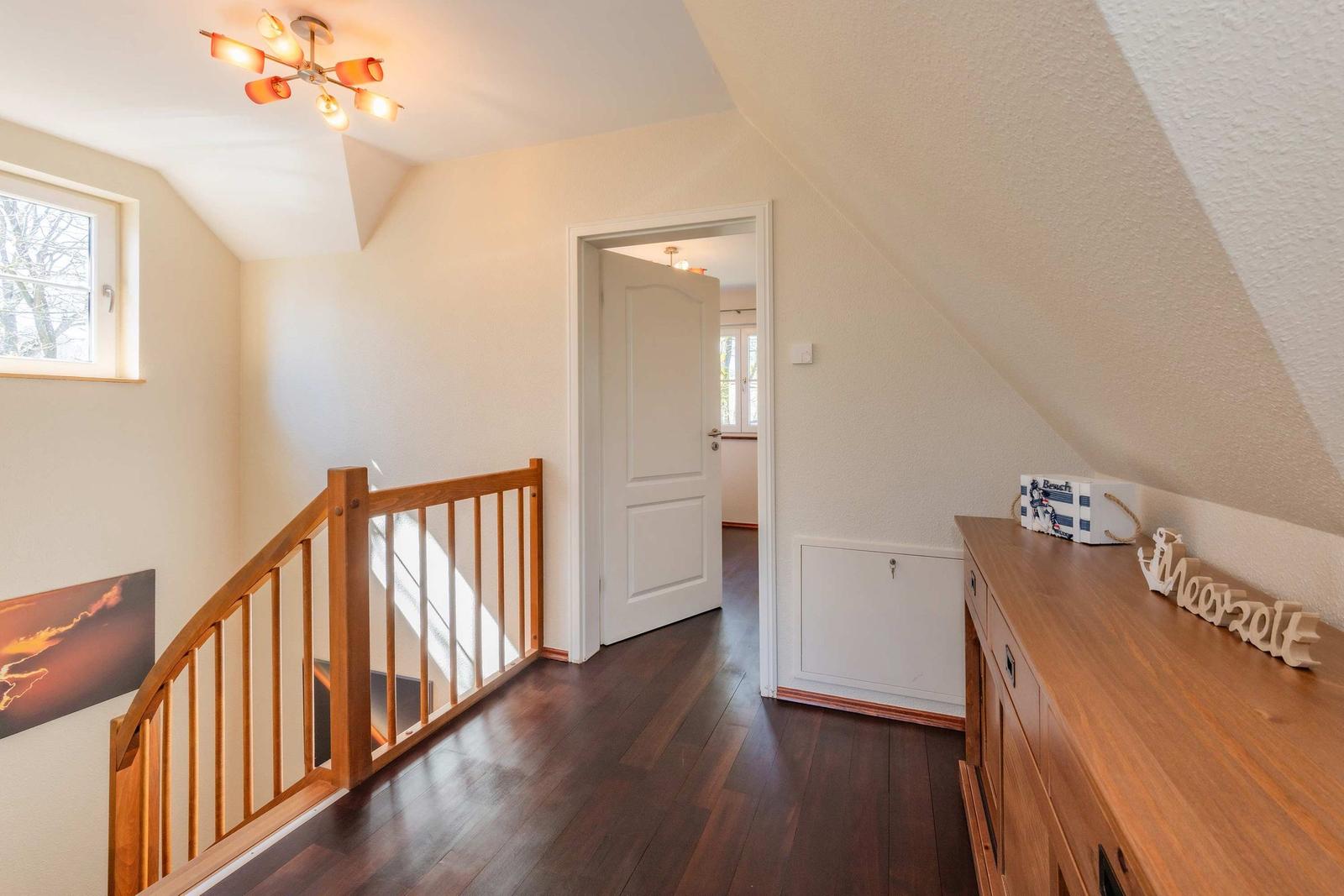 Eingangsbereich mit Holztreppe, dunklem Holzboden und Schrank. Dachgeschoss mit Fenster und Deckenleuchte.