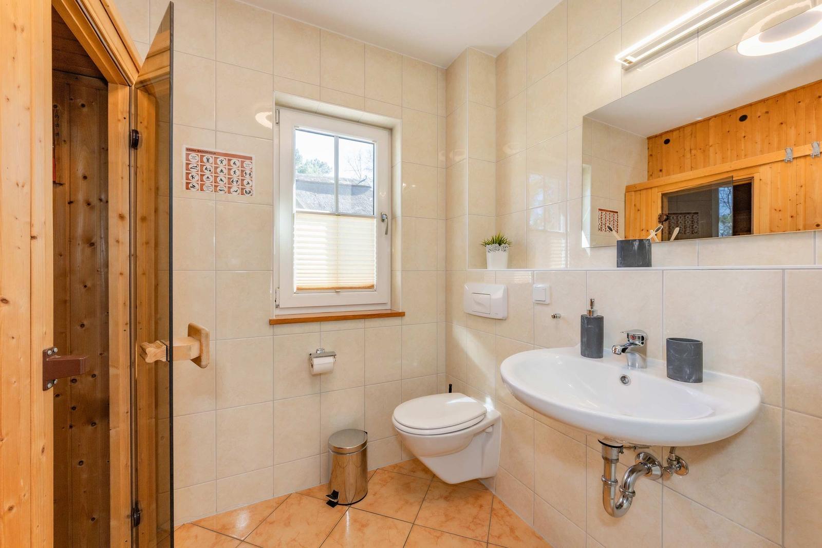 Bad mit Dusche, Waschbecken und Toilette. Fenster mit Jalousie.