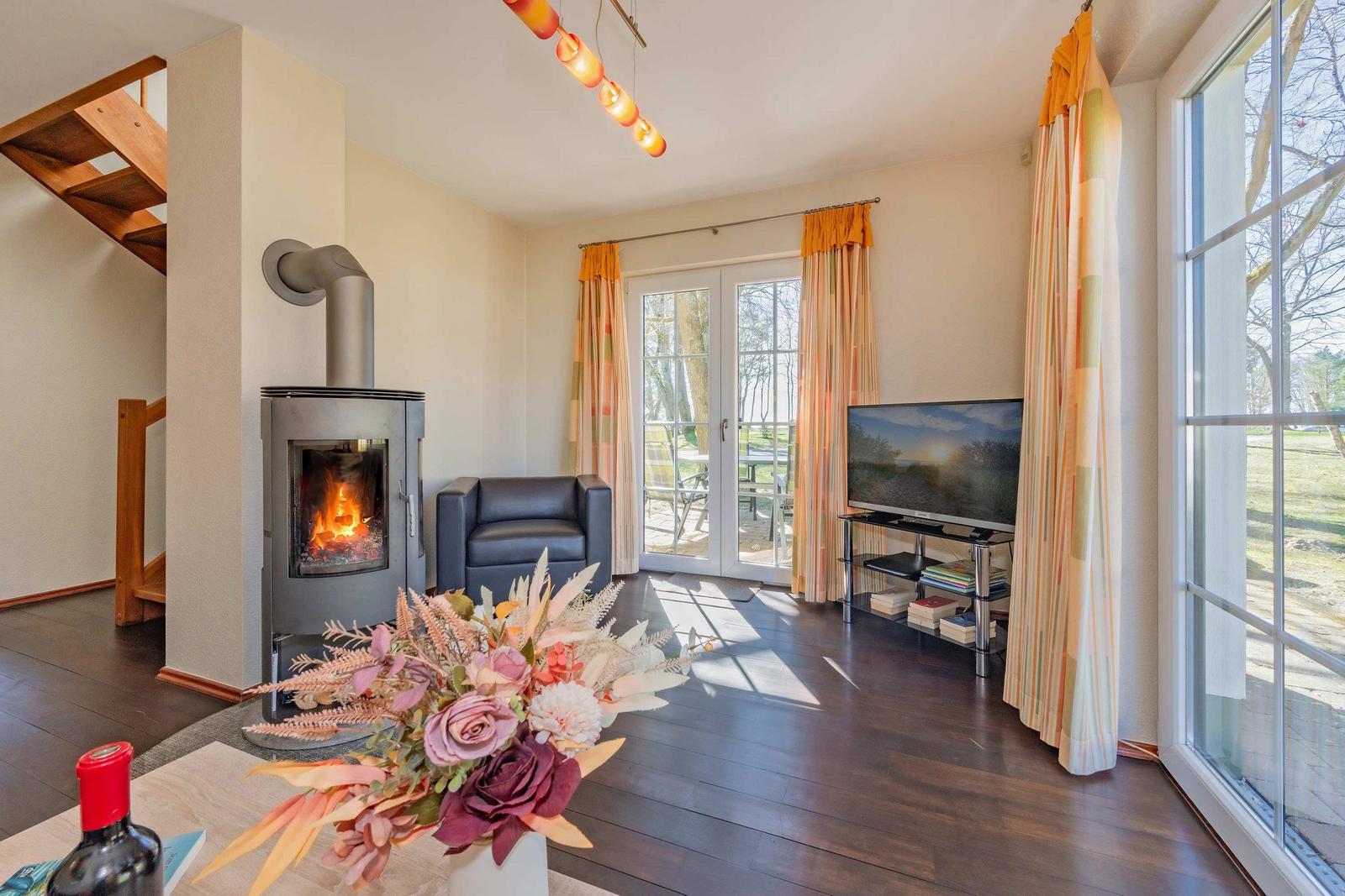 Wohnzimmer mit Kamin, TV und Terrasse. Holzboden und große Fenster.