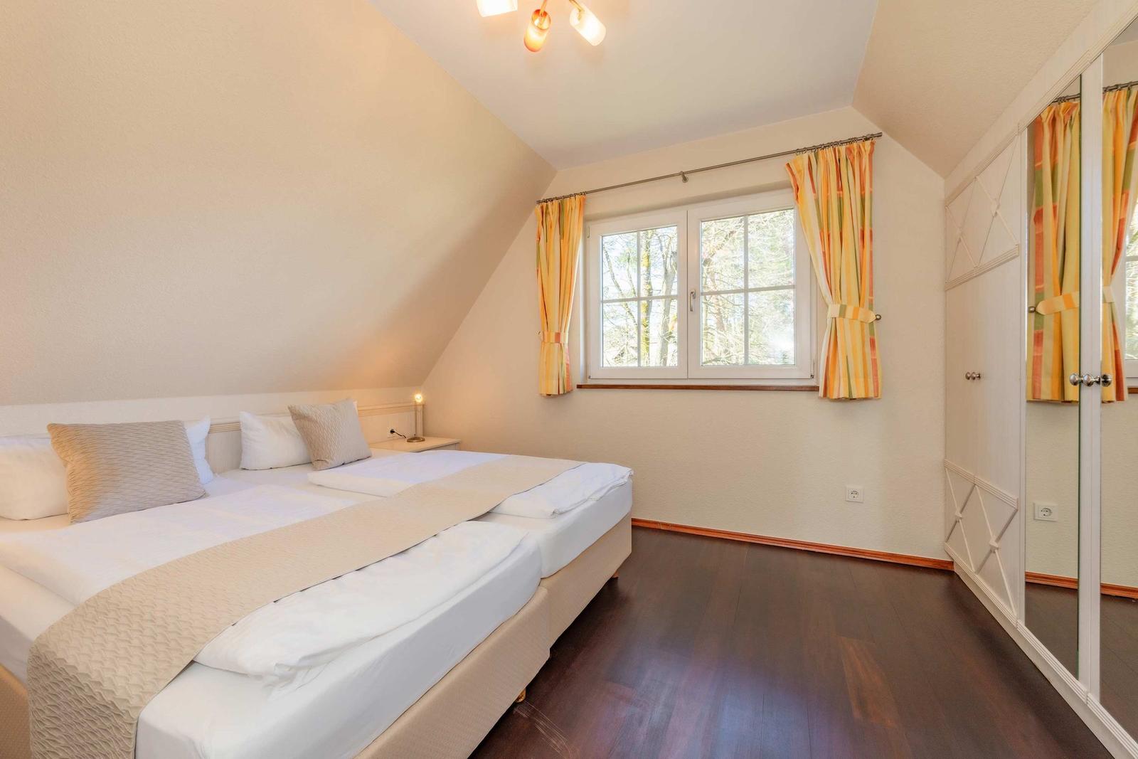 Schlafzimmer mit Doppelbett, Fenster und Kleiderschrank.