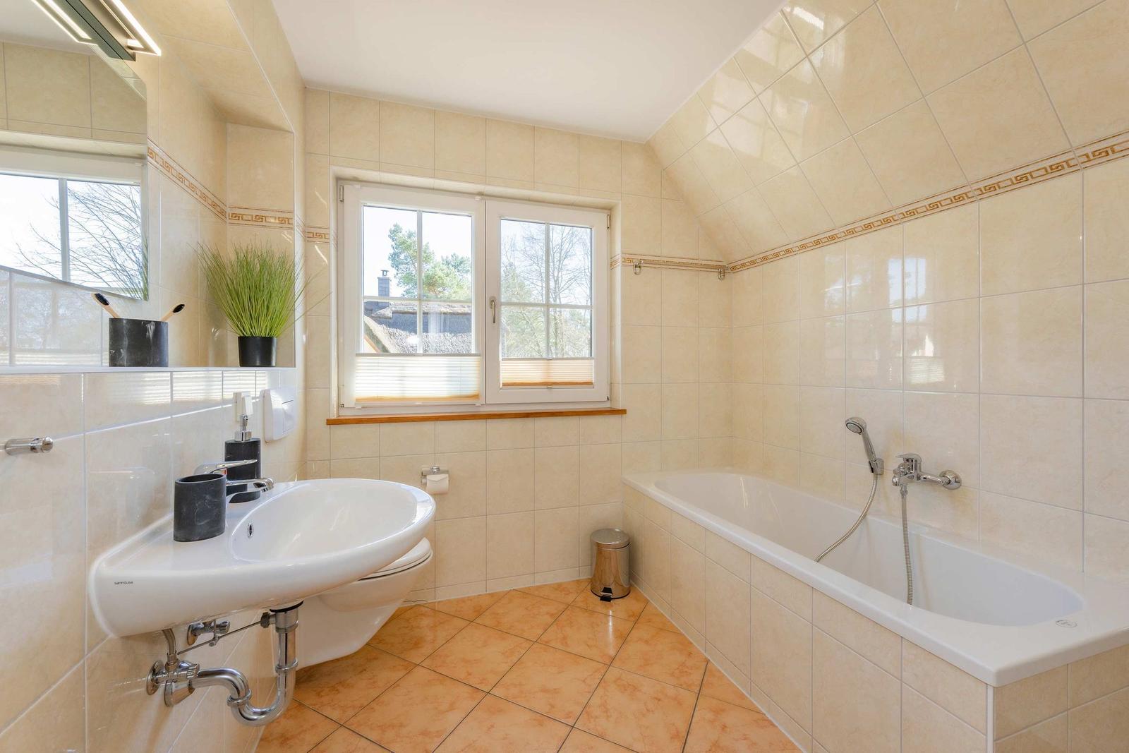 Badezimmer mit Badewanne, Waschbecken und Fenster. Wand- und Bodenfliesen.