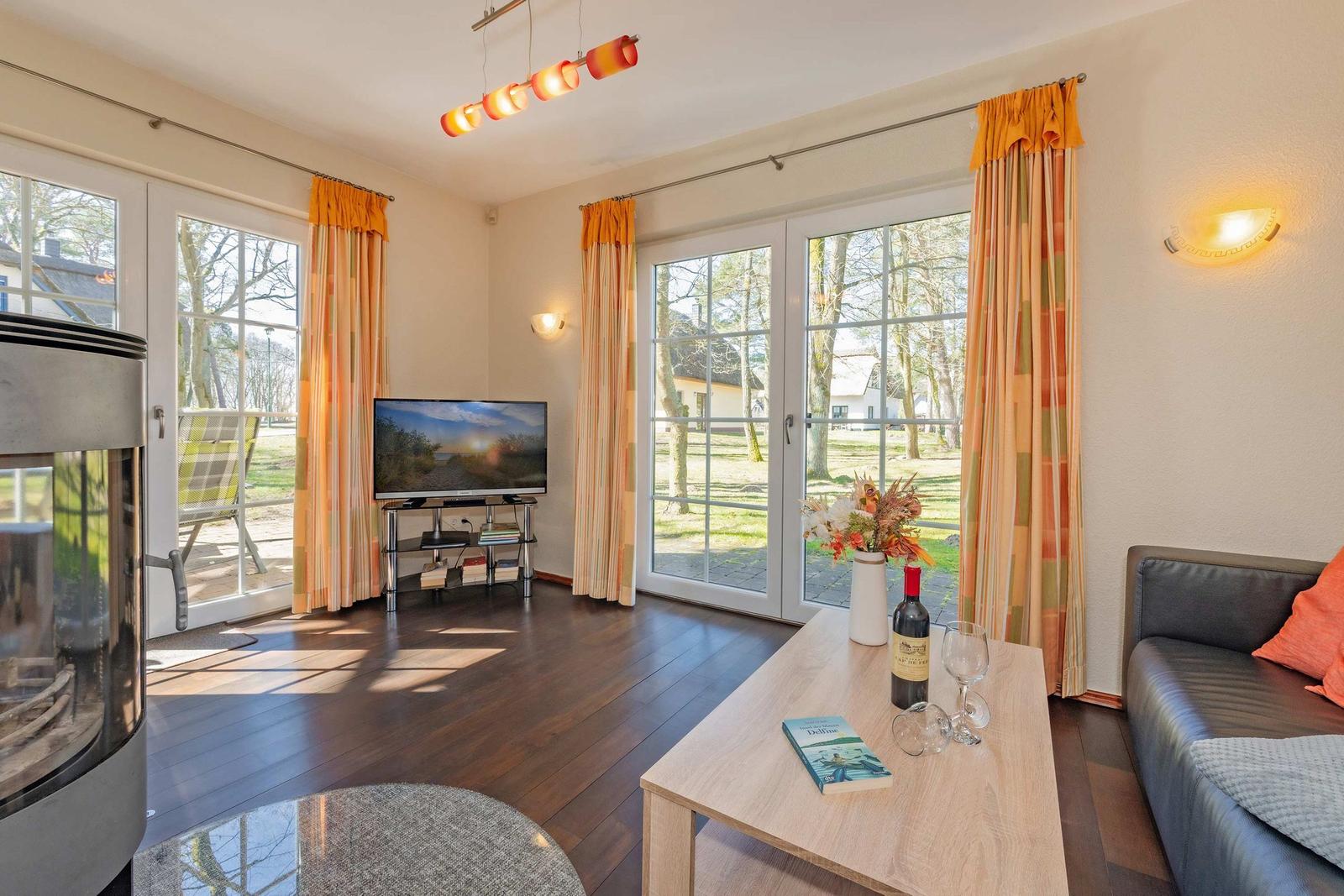 Wohnzimmer mit Sofa, Fernseher und Terrassentüren mit orangefarbenen Vorhängen.