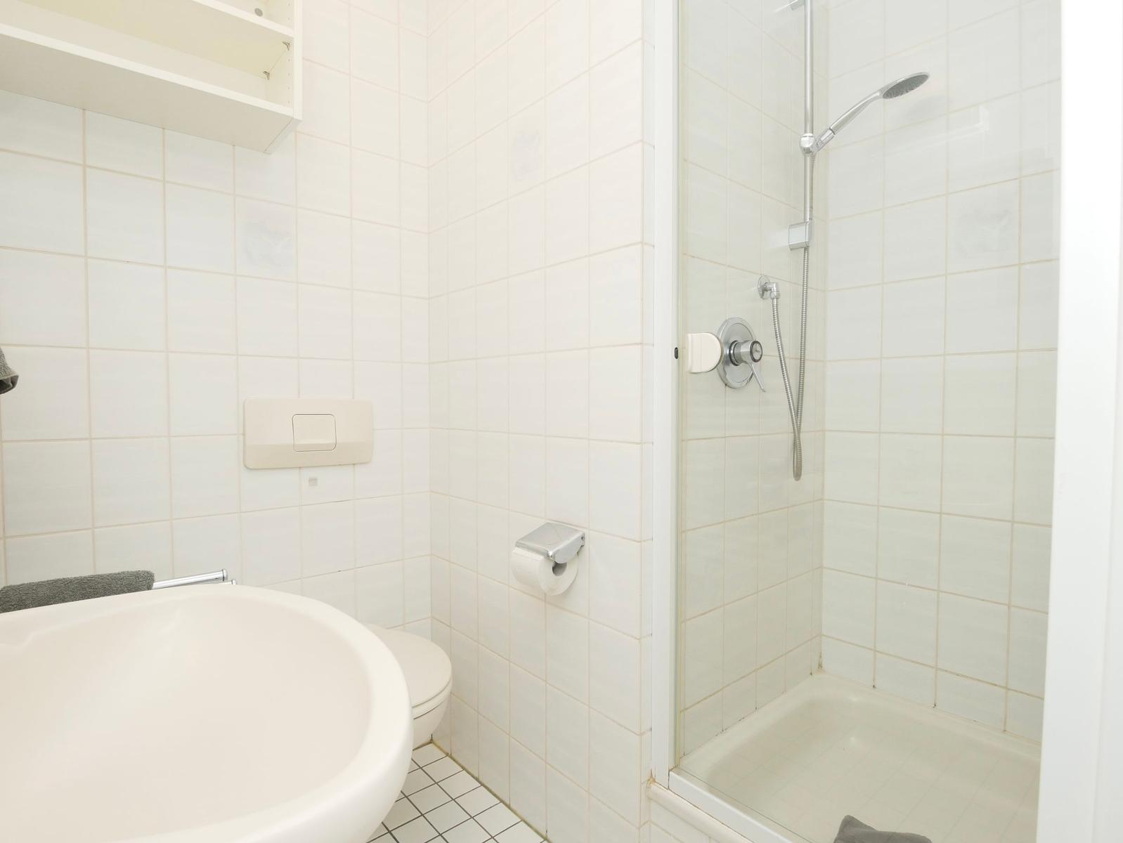 Badezimmer mit Dusche, Waschbecken und Toilette. Weiße Fliesen und moderne Armaturen.