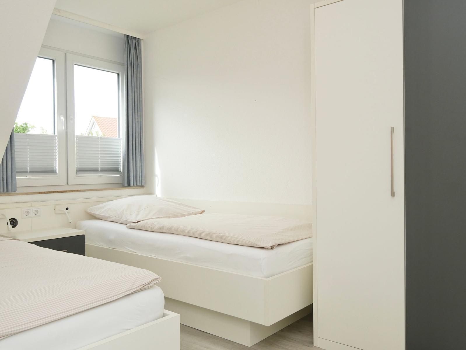 Zwei Betten, Fenster mit Jalousien und Kleiderschrank im Schlafzimmer.