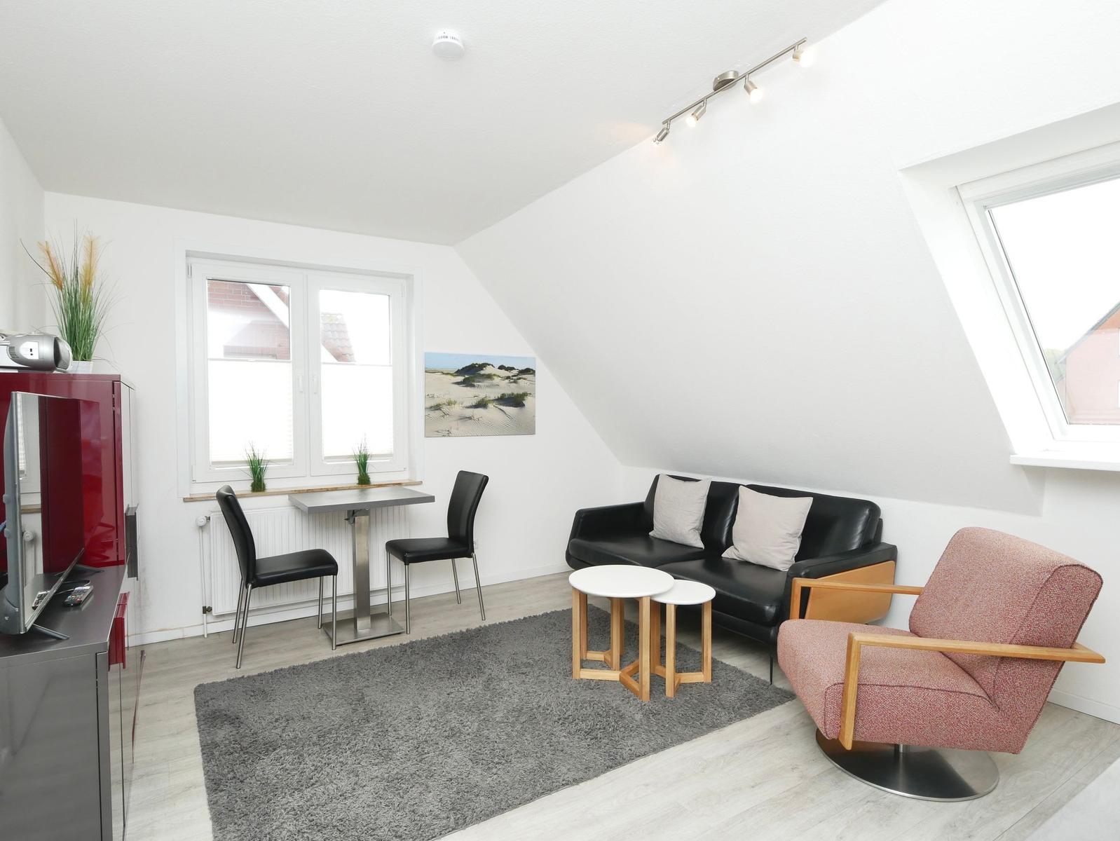 Wohnzimmer mit Sofa, Sessel, Tisch und Fenstern