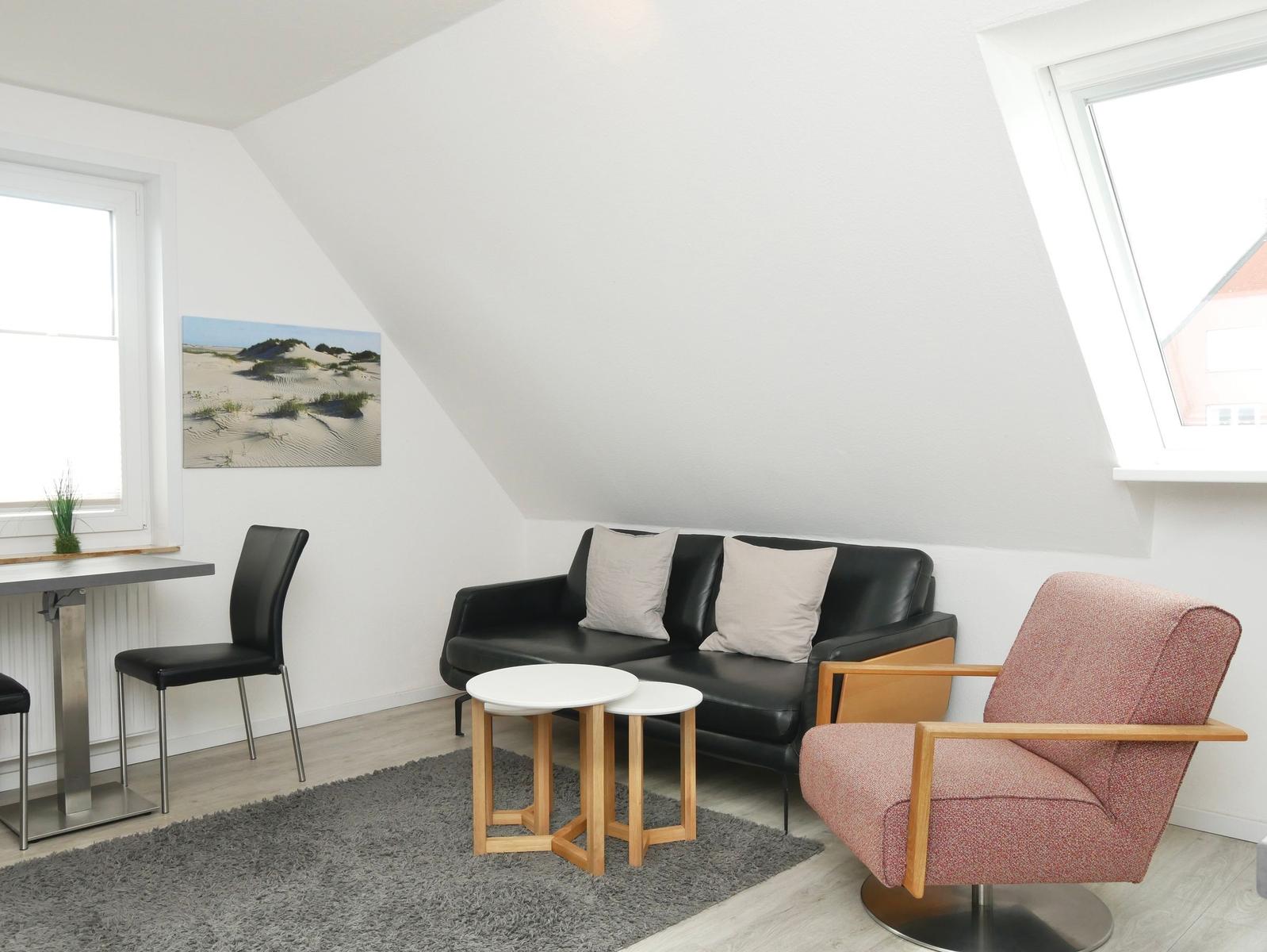 Wohnraum mit Sofa, Sessel und Tisch unter Dachschrägen.