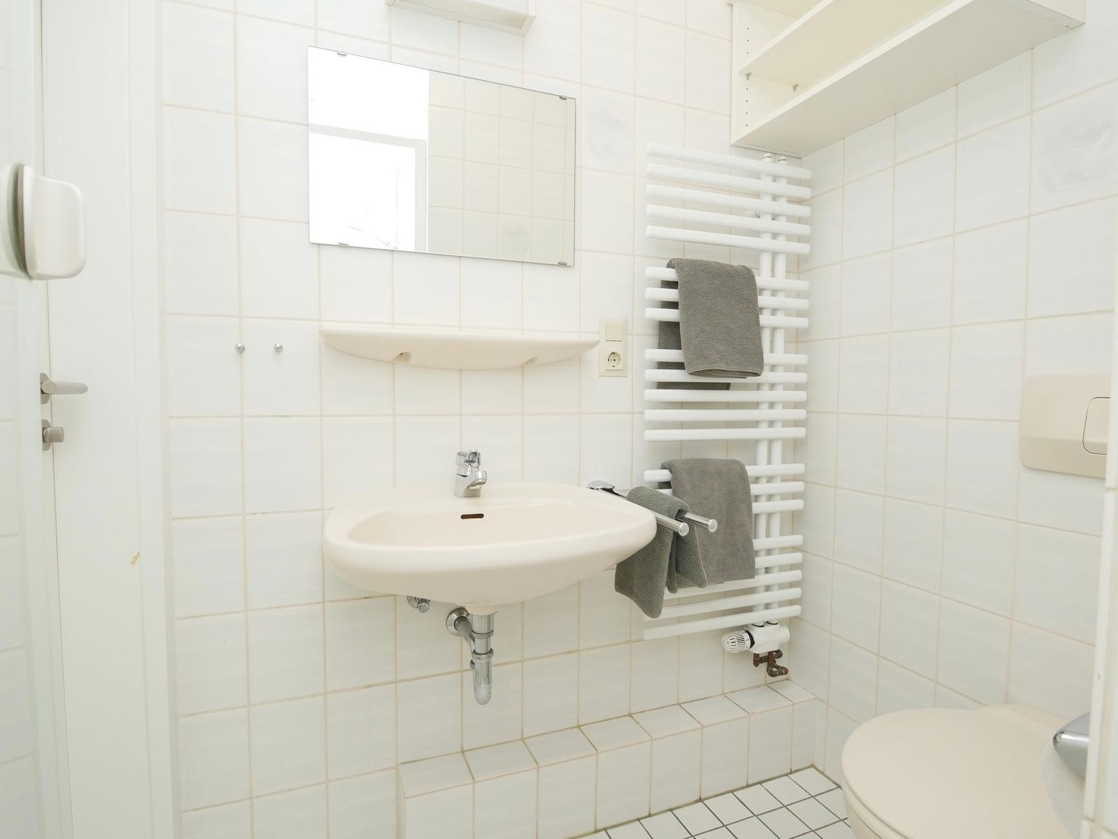 Badezimmer mit Waschbecken, Spiegel, Handtuchhalter und Toilette.