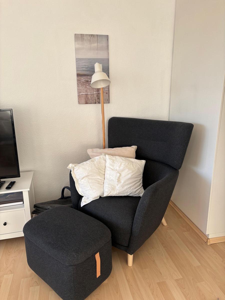 Schwarzer Sessel mit Kissen und Hocker vor Wand mit Bild und Stehlampe.