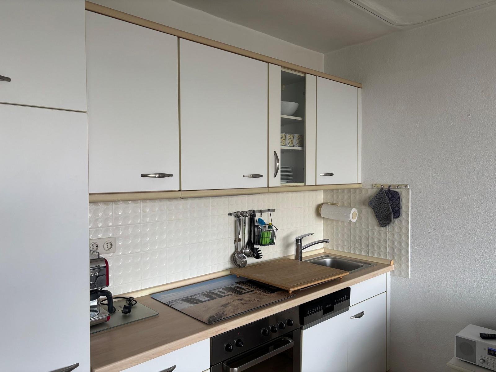 Küche mit weißen Schränken, Edelstahlspüle und Holzplatte auf Arbeitsfläche.