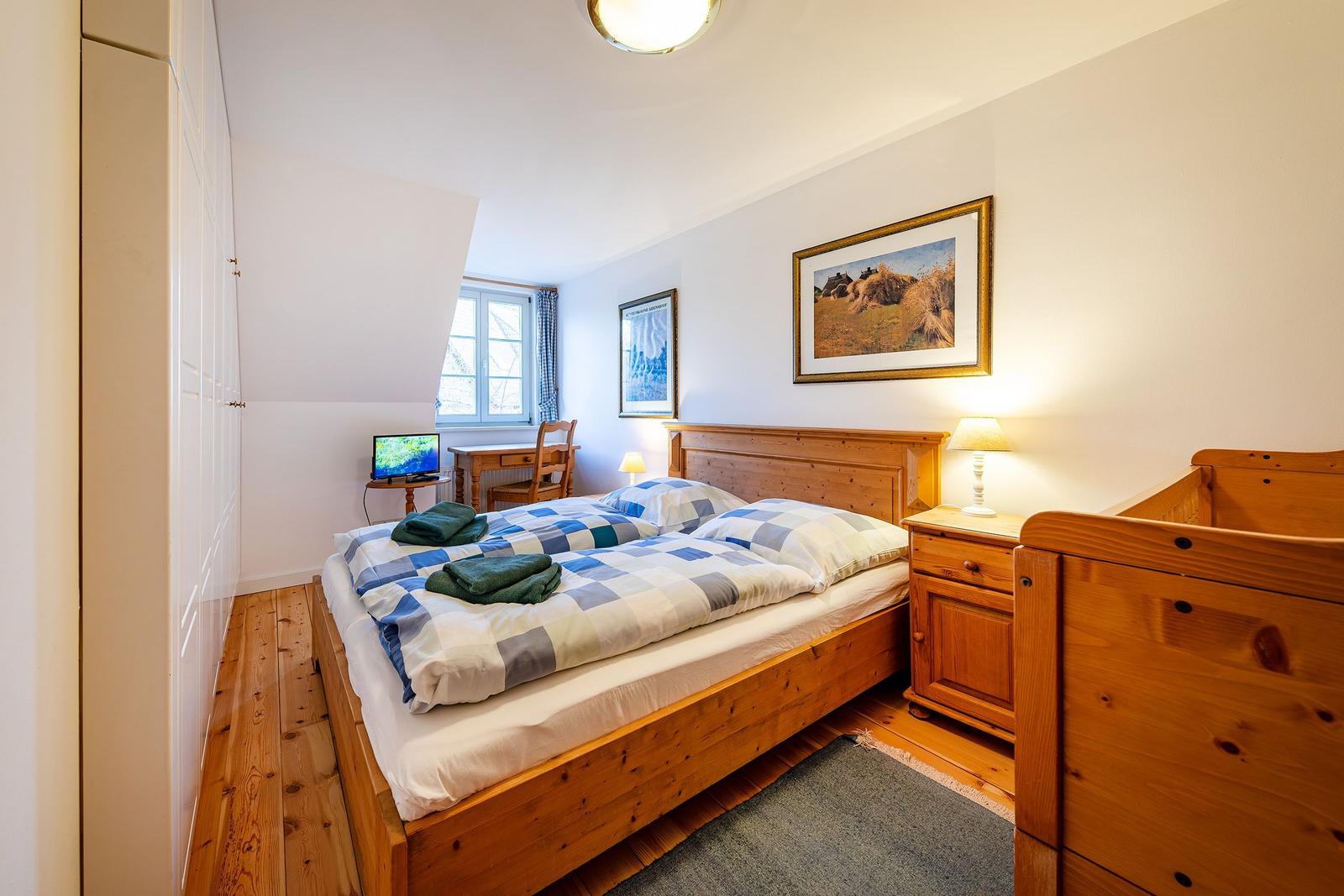 Schlafzimmer mit Holzbett, Nachttisch, Kleiderschrank und Fenster.