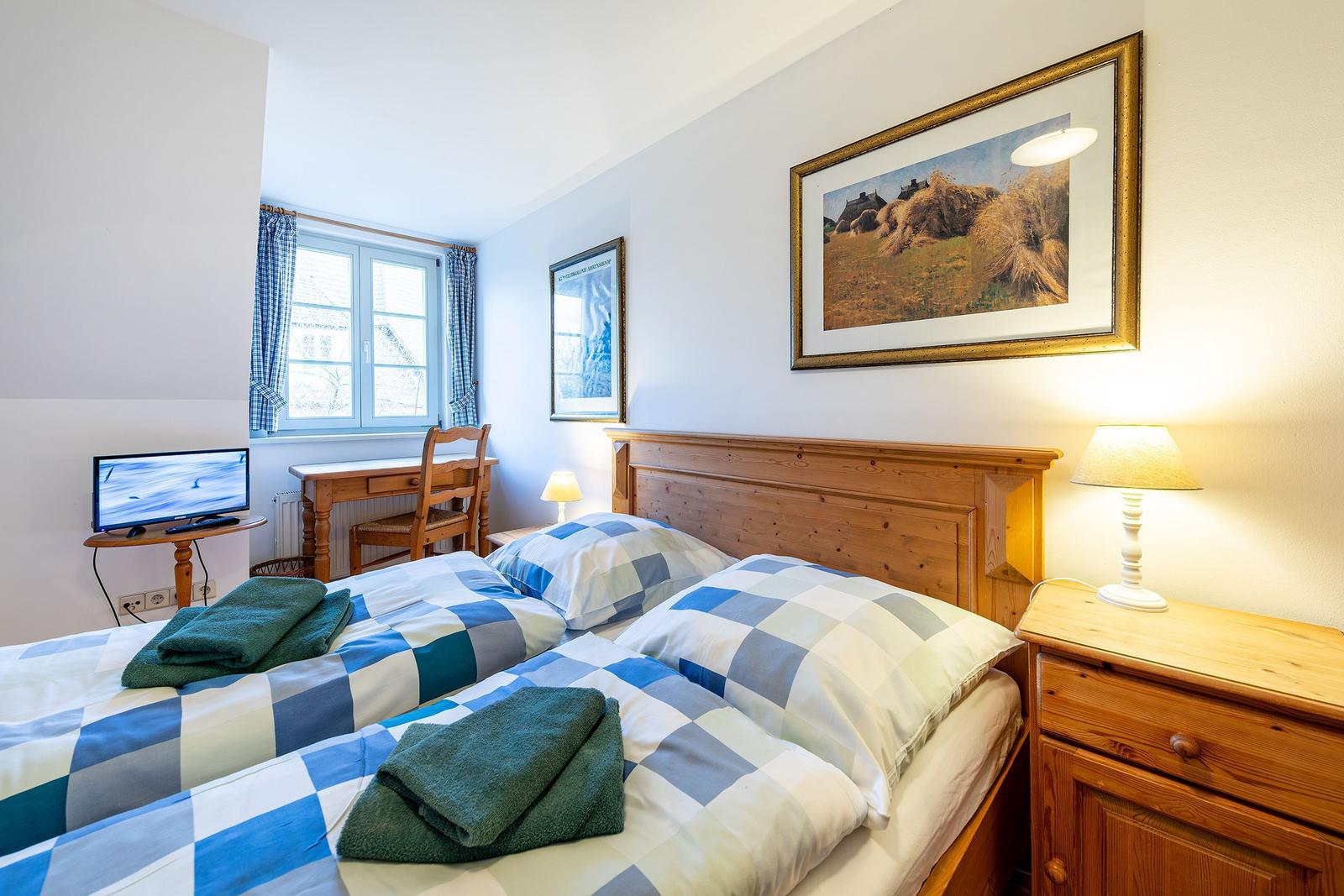 Zimmer mit Doppelbett, Schreibtisch, Fernseher und Holzmöbel.